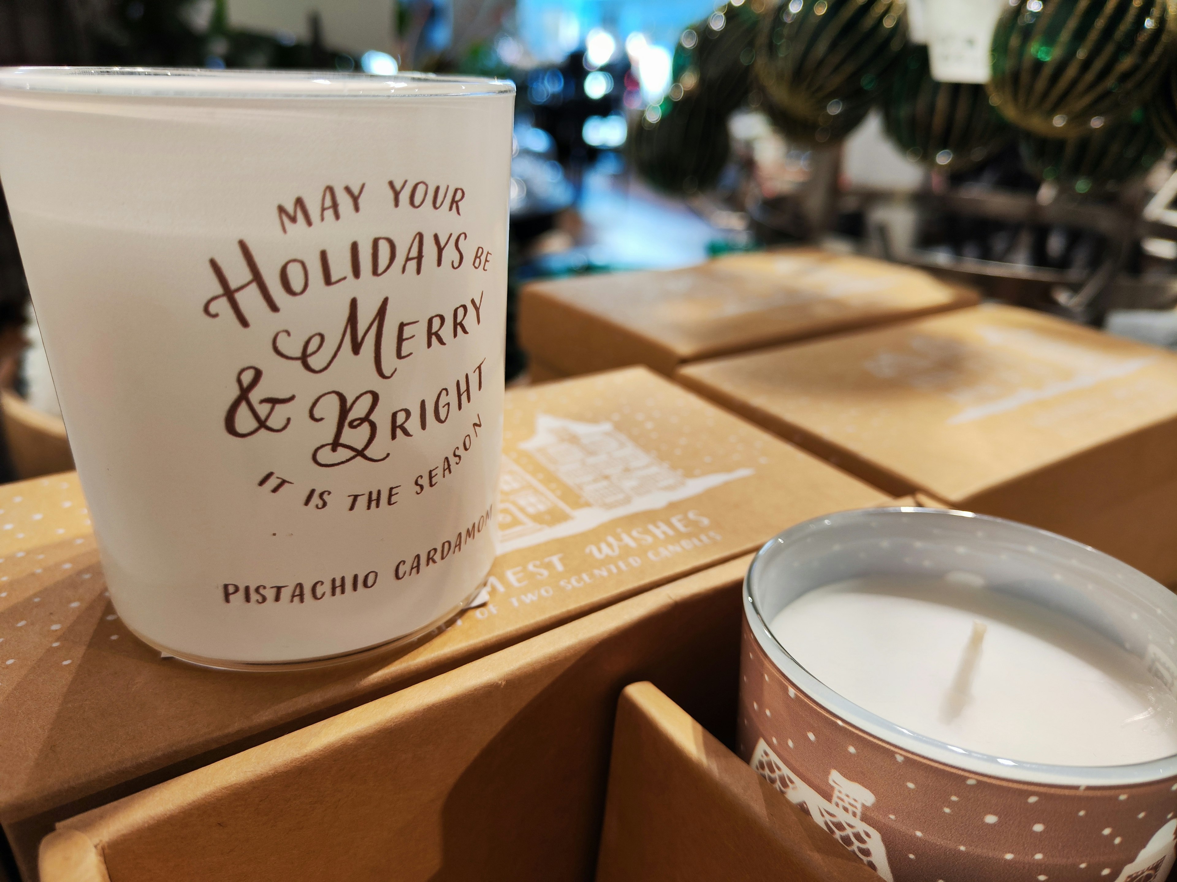 Bougie blanche avec le texte Que vos vacances soient joyeuses et lumineuses placée sur des boîtes en carton