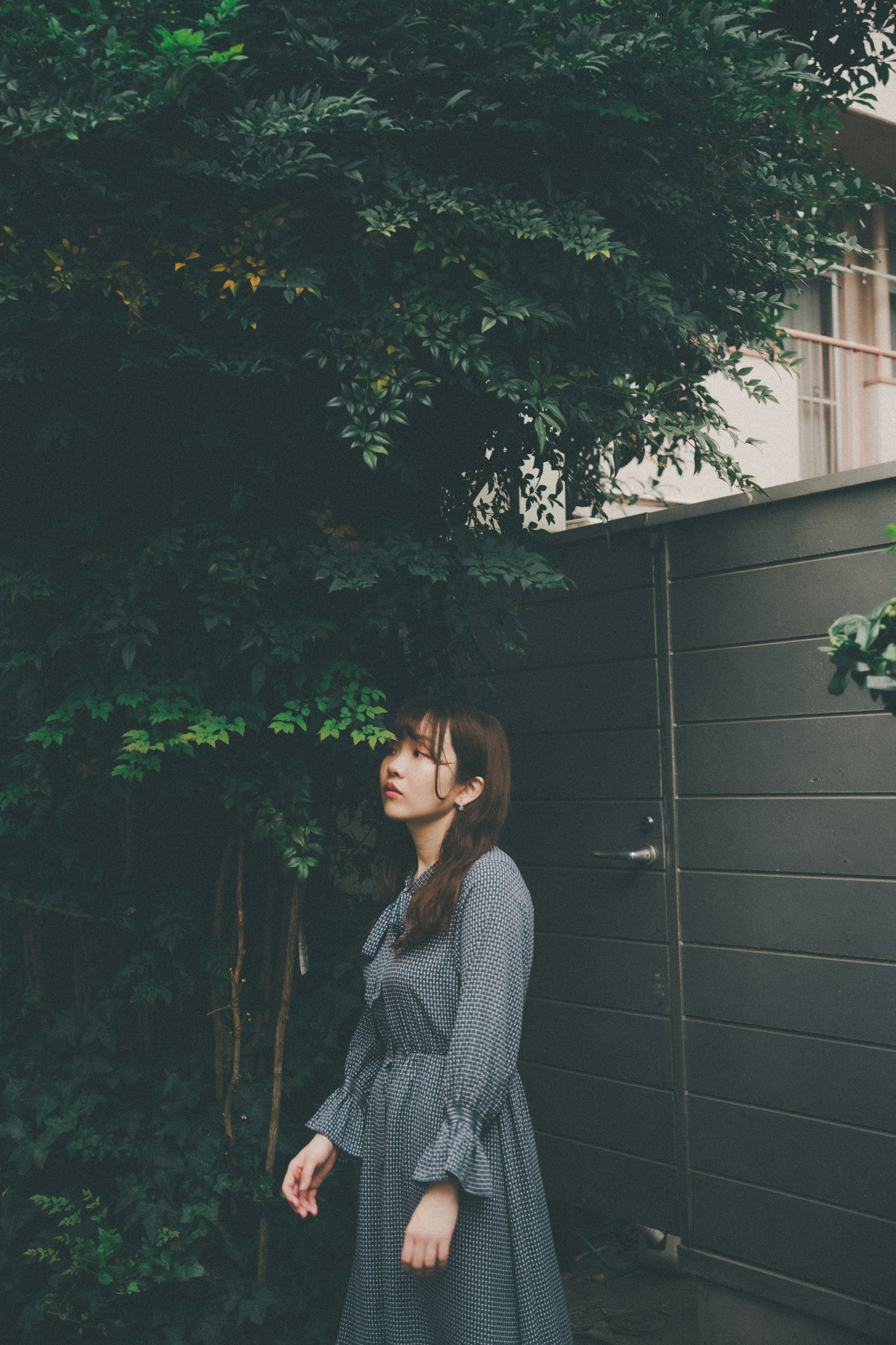 A woman in a gray dress standing among green trees