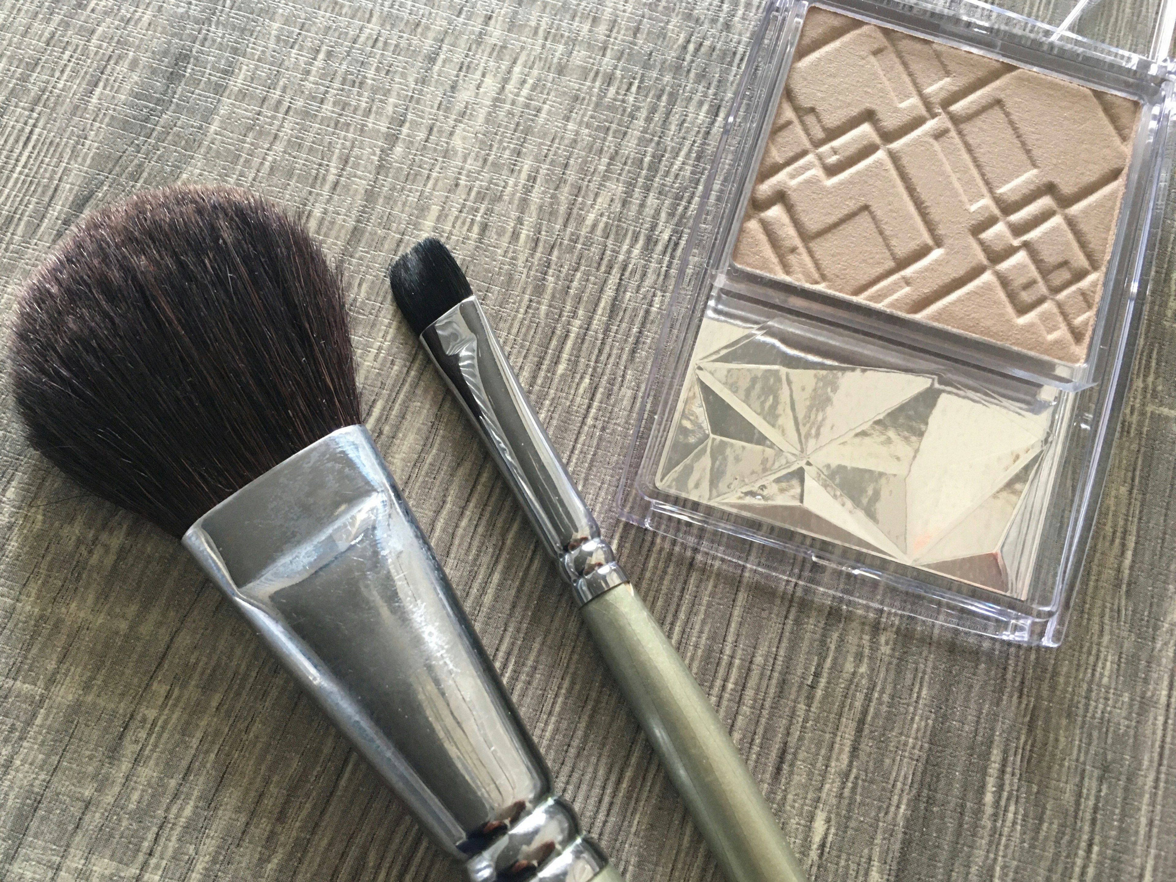 A set of makeup brushes and highlighter powder placed on a wooden table