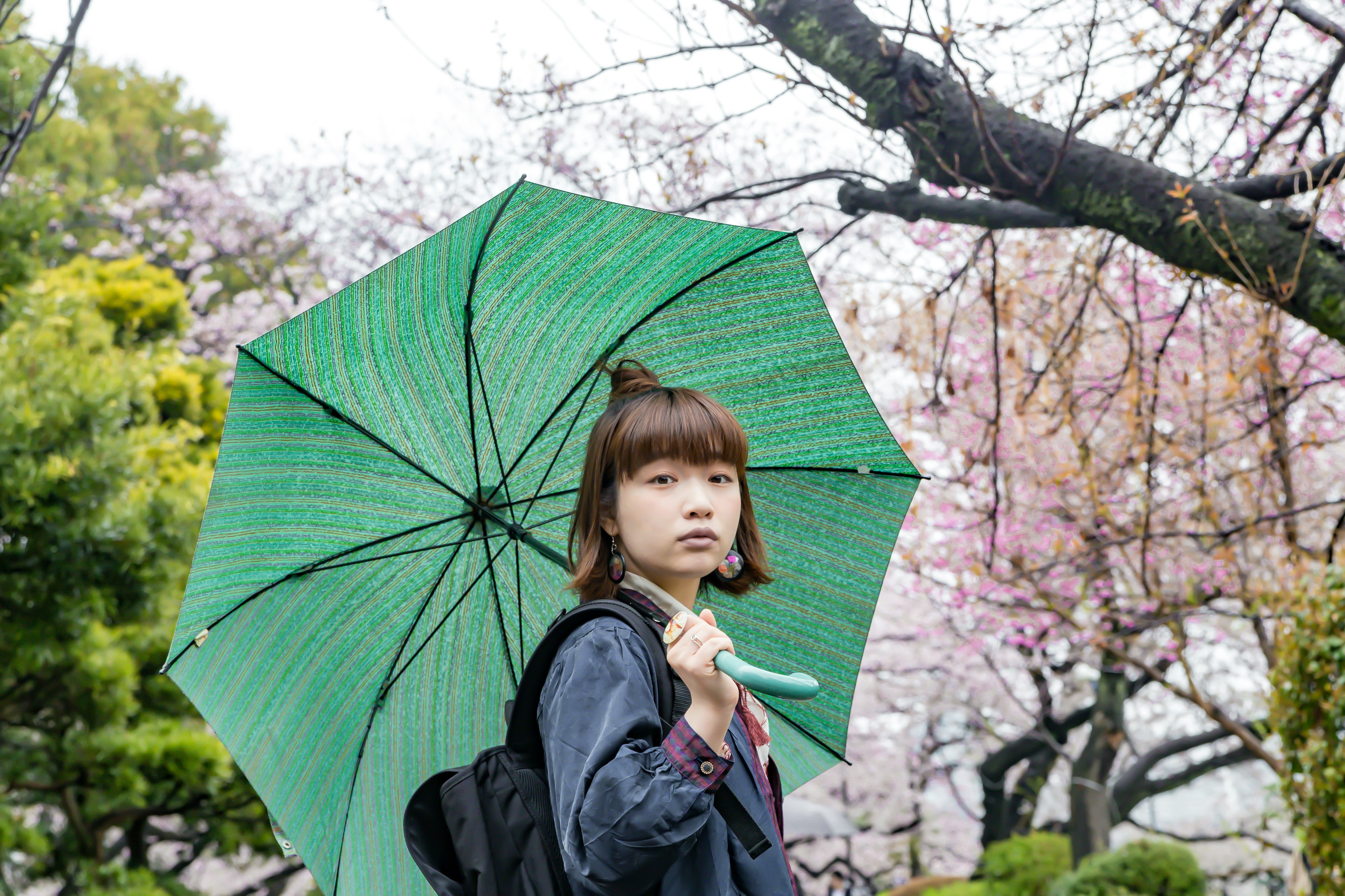 年轻女性手持绿色雨伞站在樱花树旁