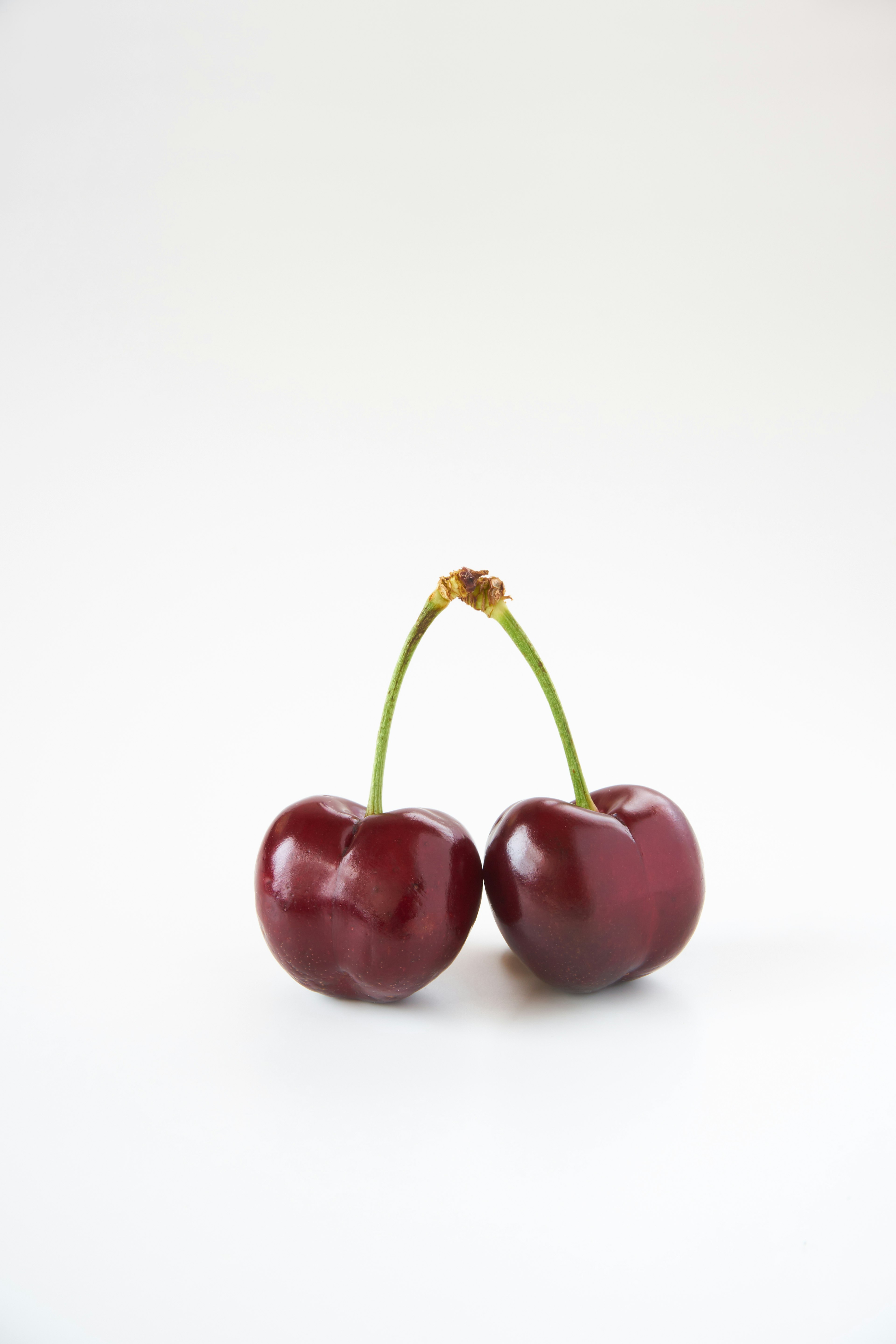 Two red cherries with green stems on a white background