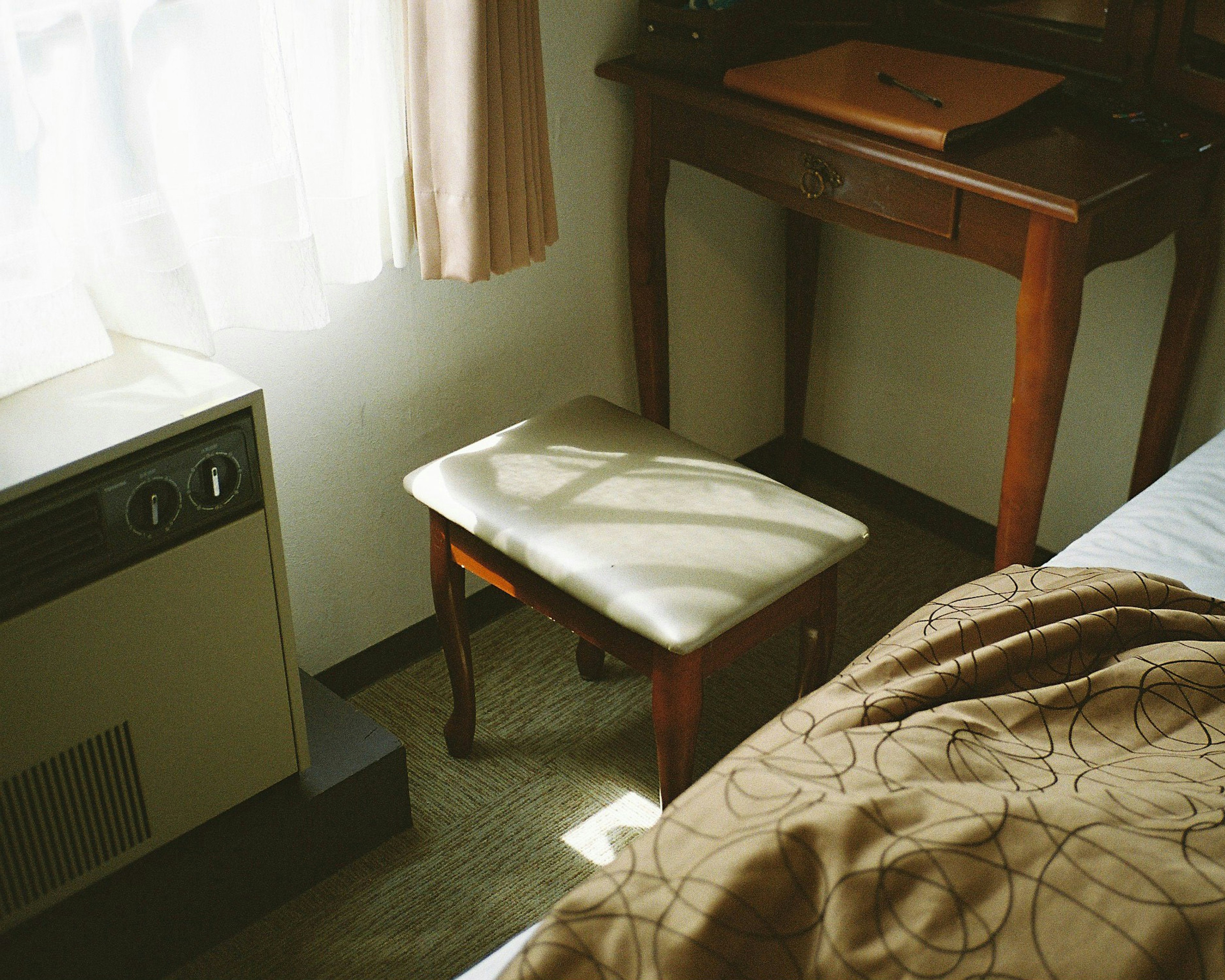 A corner of a room featuring a wooden table and stool with natural light streaming in from the window