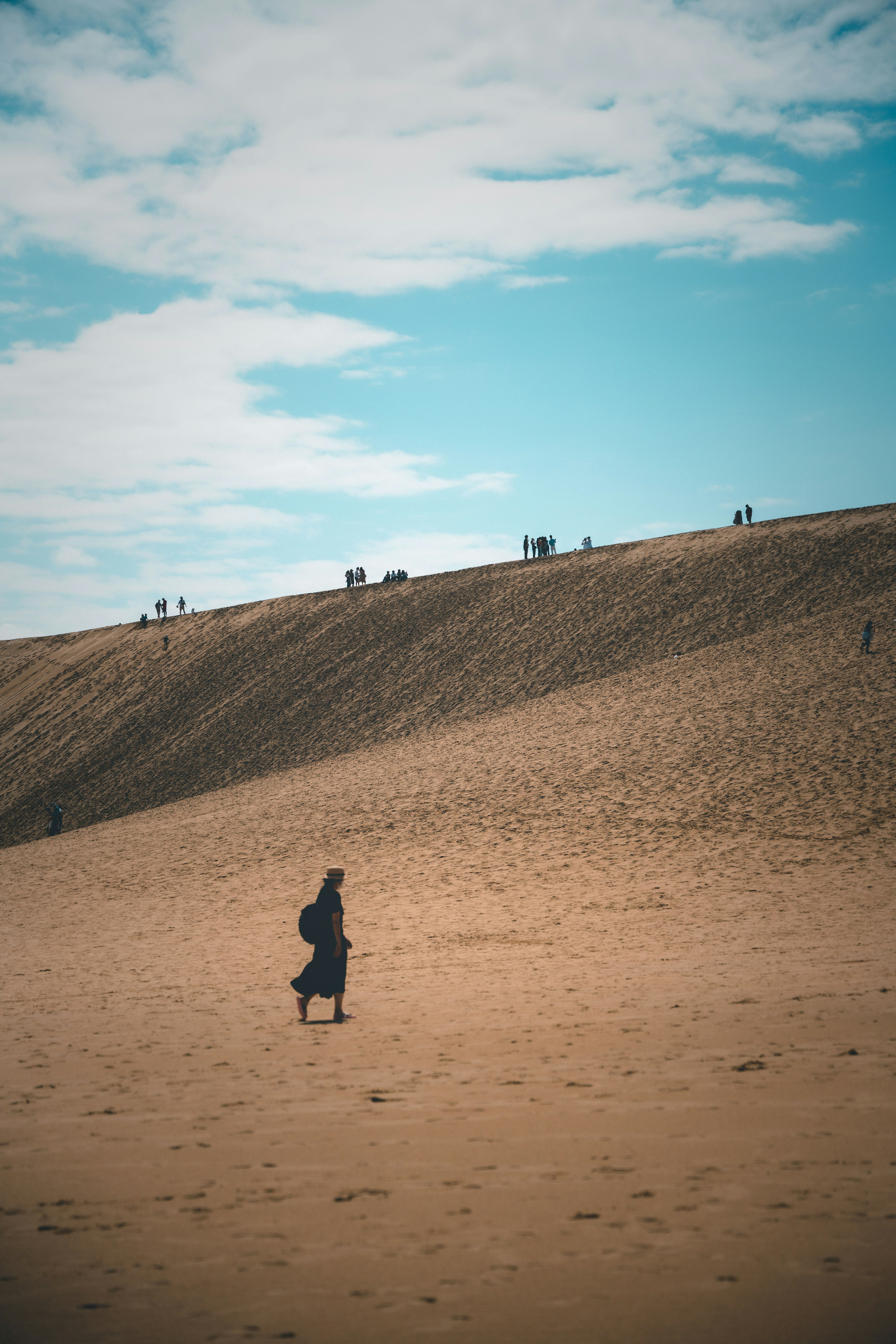 Una persona caminando sobre una duna de arena bajo un cielo azul