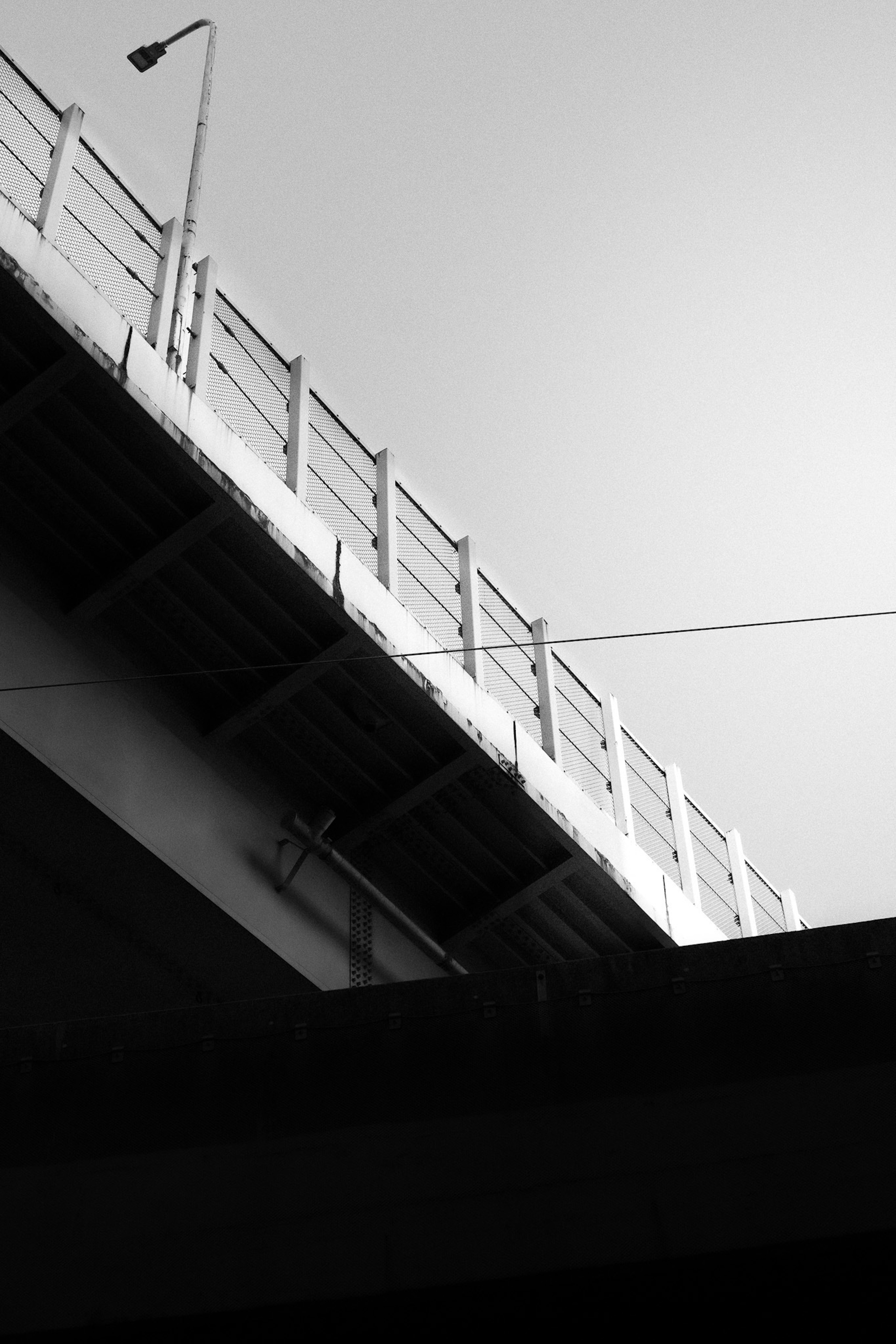 Vista en blanco y negro de un puente desde abajo con barandilla y farola visibles