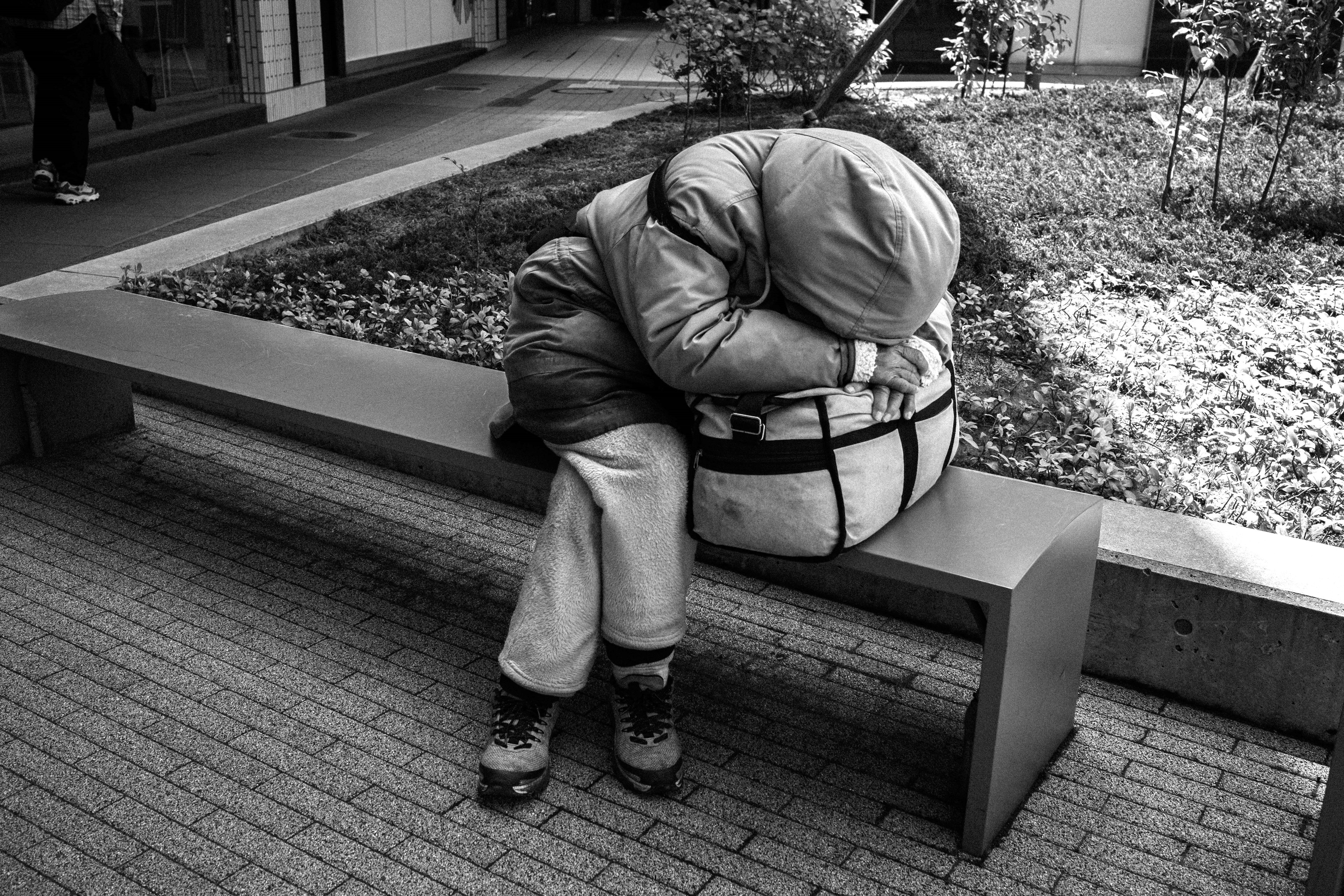 A child huddled on a park bench wearing warm clothing