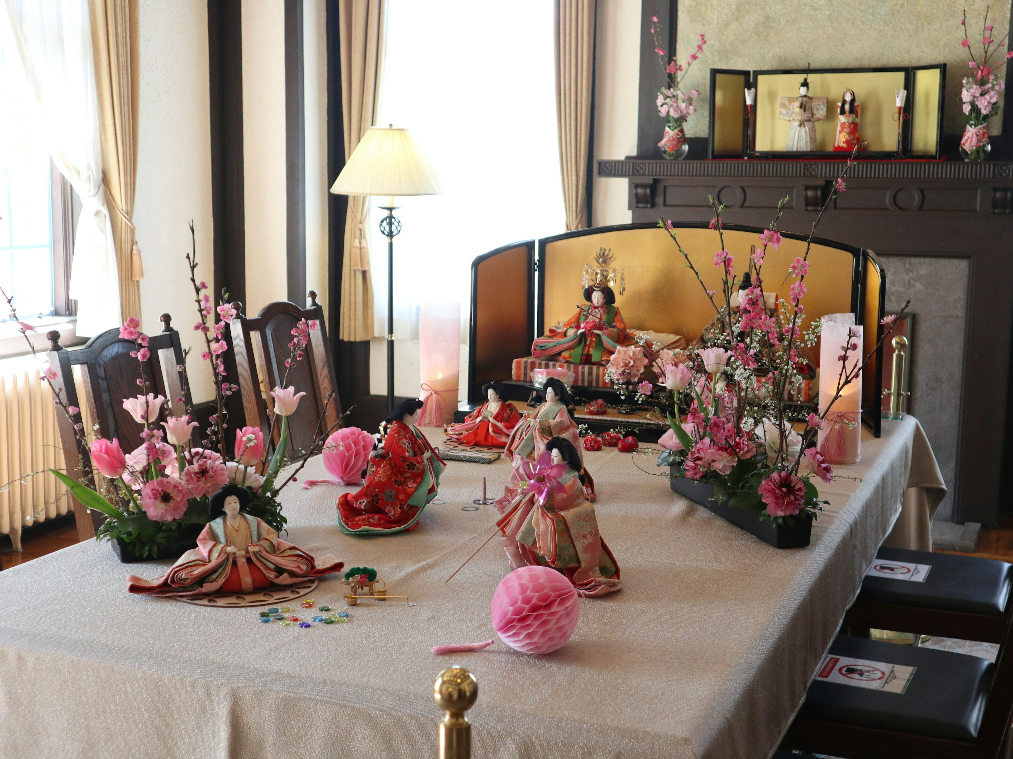 Room decorated for Hinamatsuri with vibrant hina dolls and pink flowers on the table