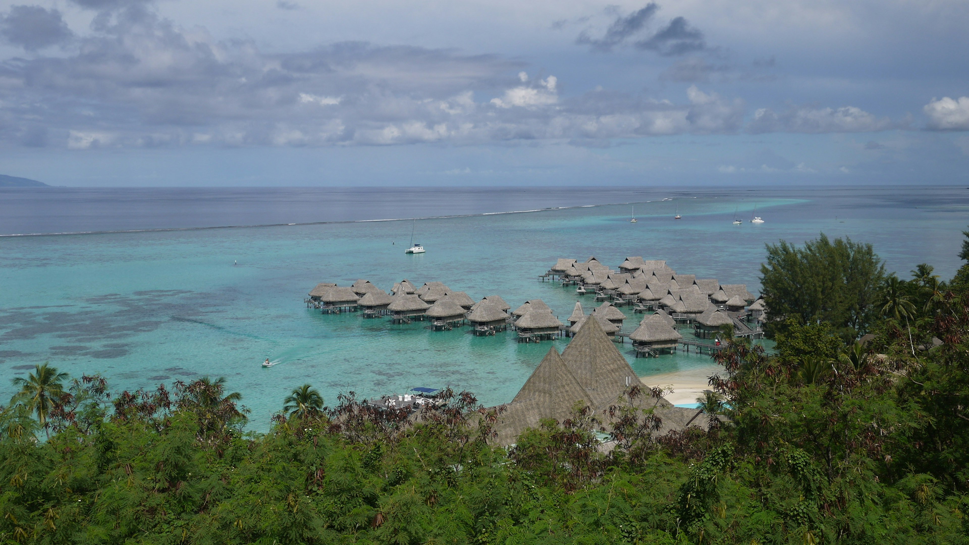 Eine malerische Aussicht auf ein Resort mit blauem Wasser und grünem Laub mit über Wasser gebauten Bungalows