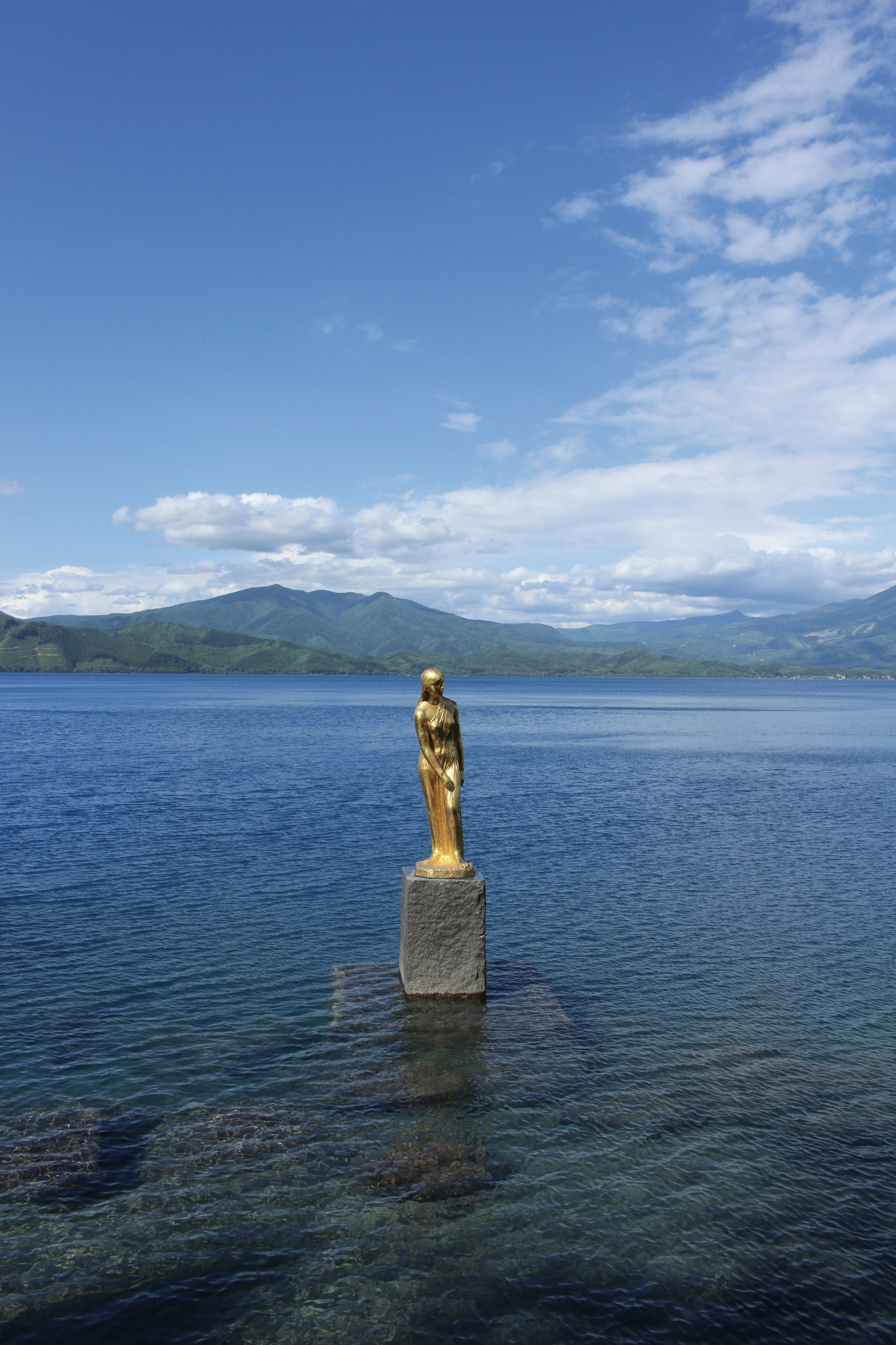 Goldene Statue steht im See mit blauem Himmel und Bergen im Hintergrund