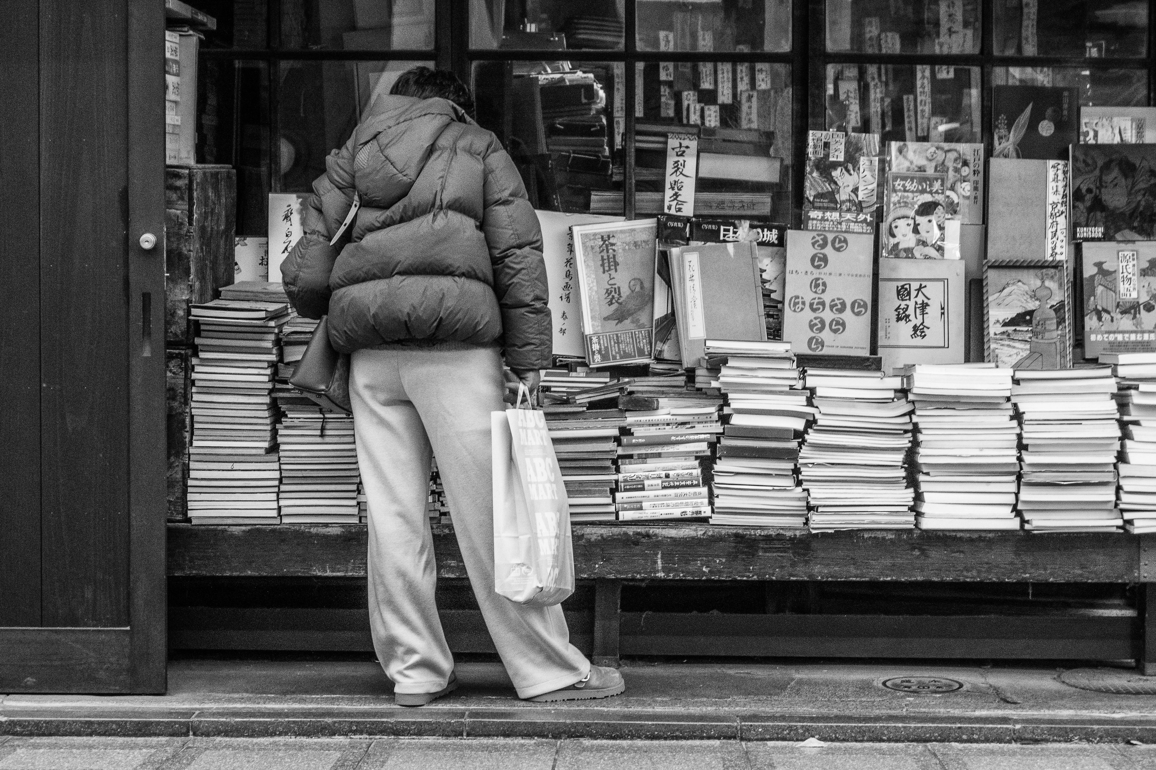 Persona de pie frente a una pila de libros en una foto en blanco y negro de una librería de calle