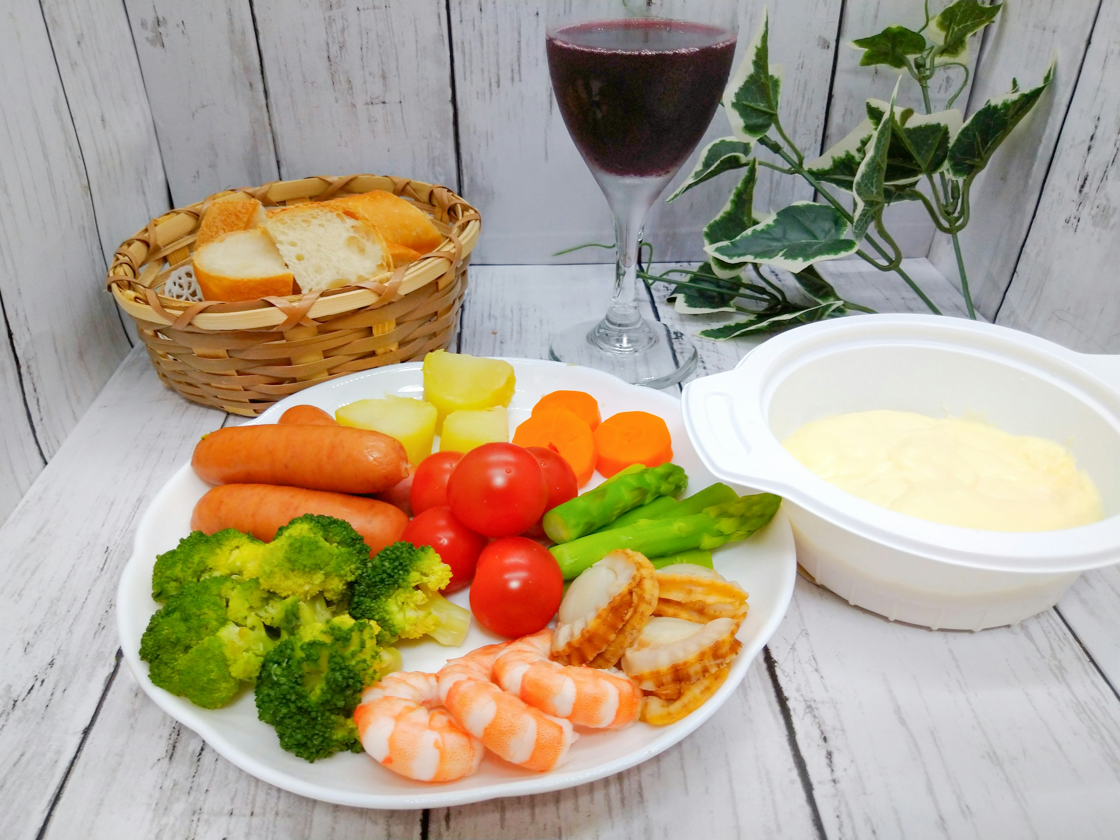 A plate with colorful vegetables and shrimp next to a basket of bread and a glass of red wine