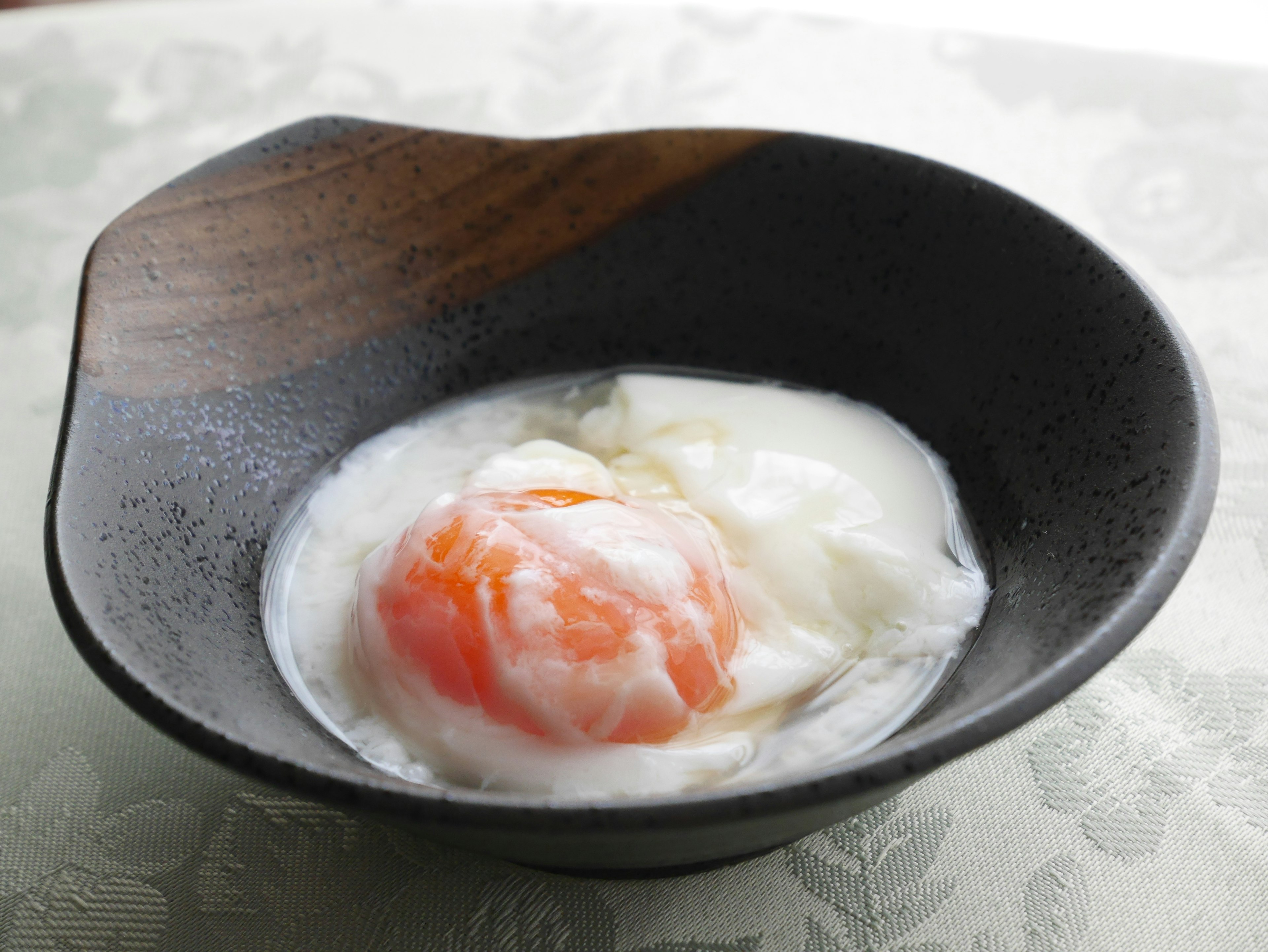 A soft-boiled egg in a black bowl with a wooden handle