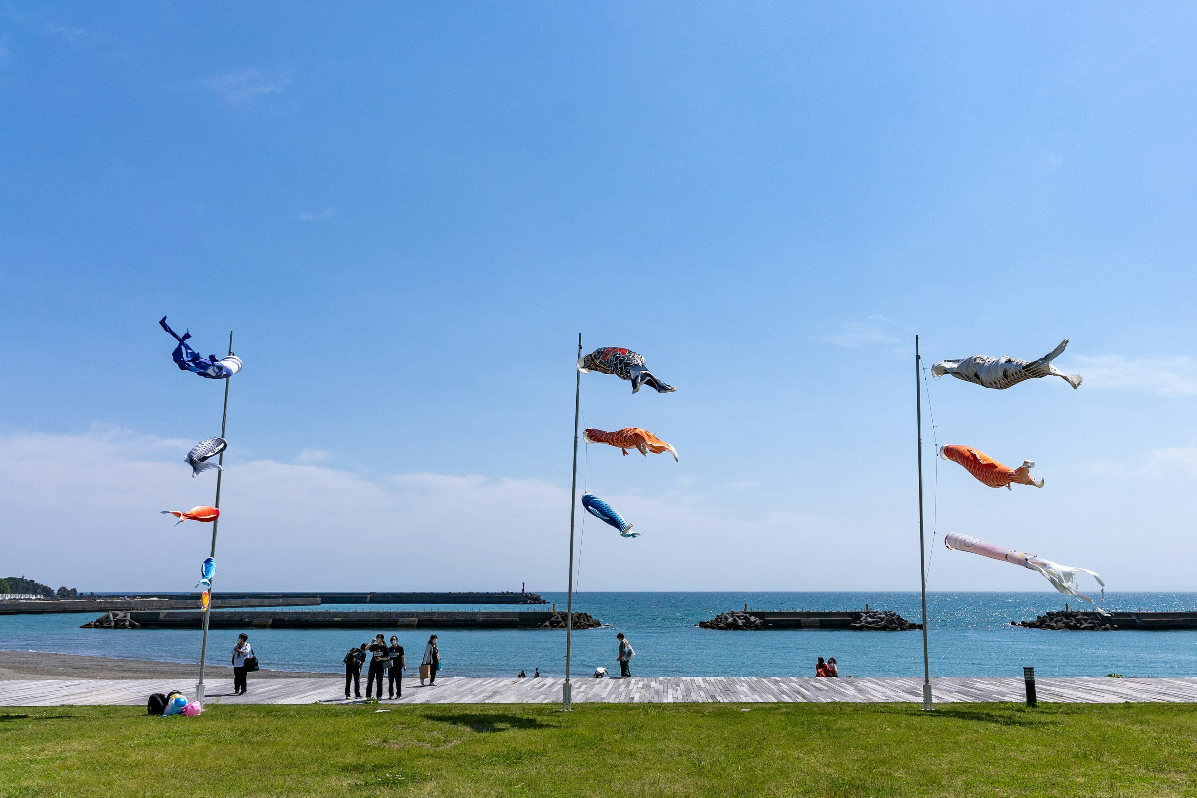 Drapeaux de poissons colorés exposés près de la mer sous un ciel bleu avec des gens observant