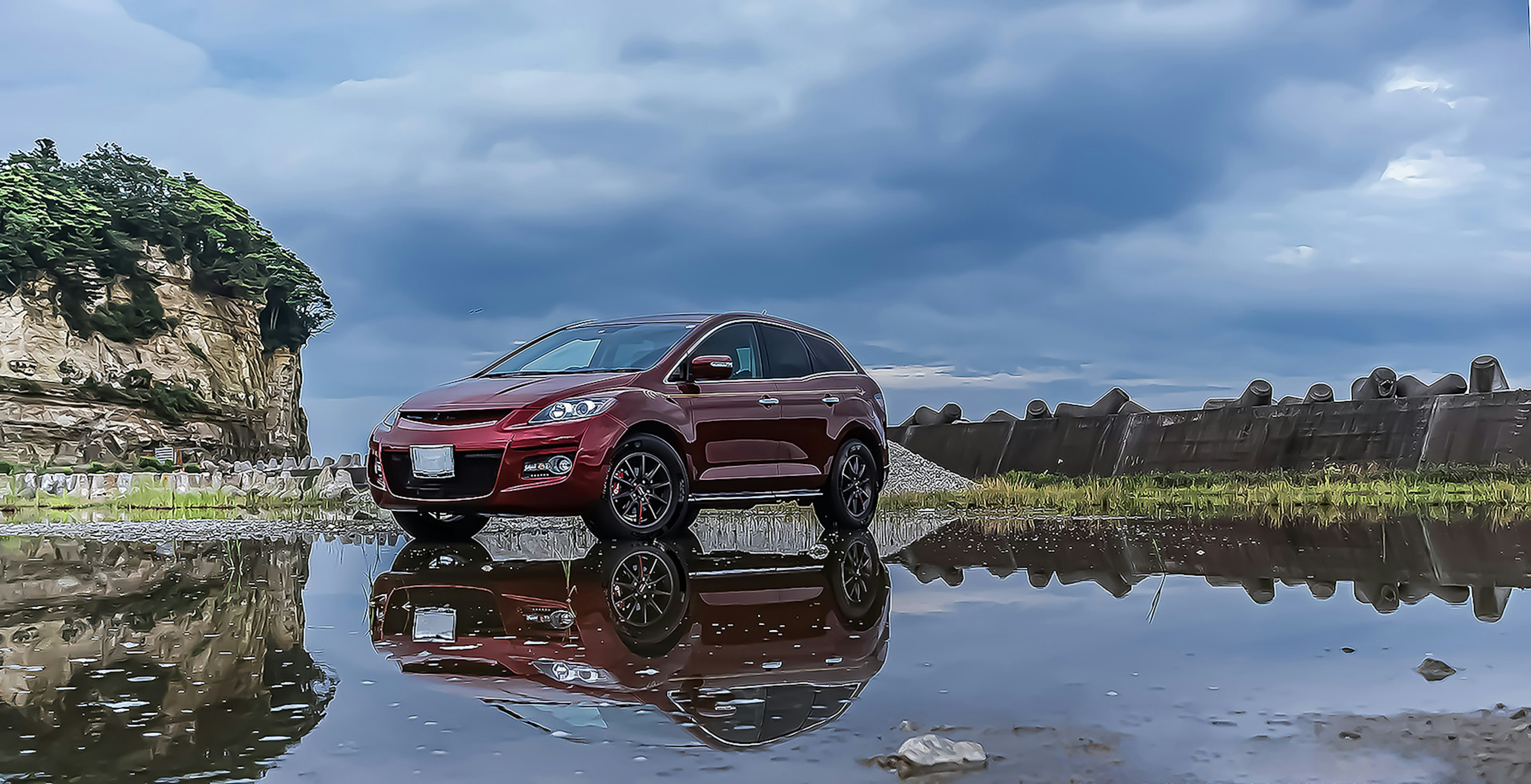 Roter SUV spiegelt sich in einer Pfütze mit dramatischen Wolken