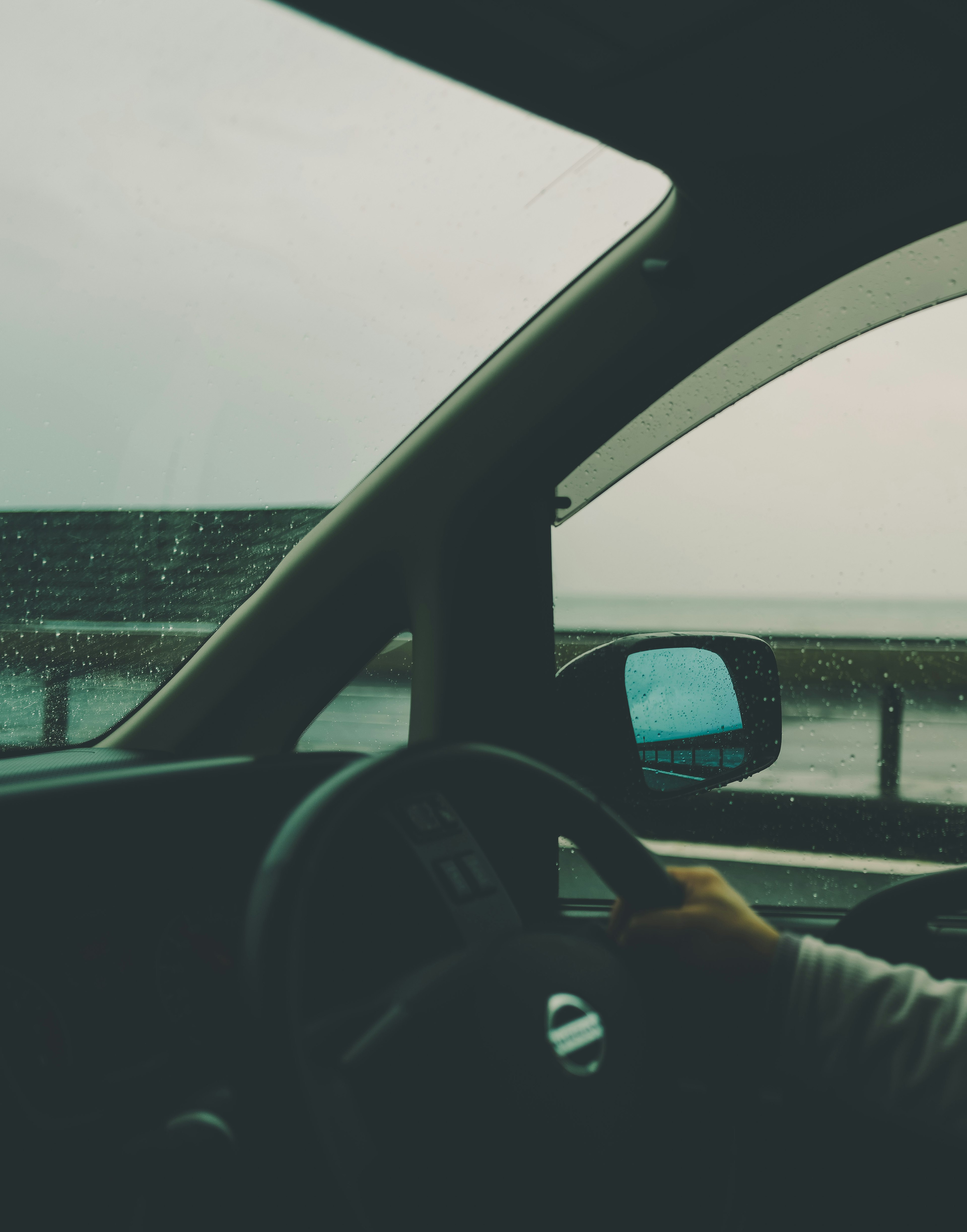 Hand on steering wheel inside a car with rain on the window