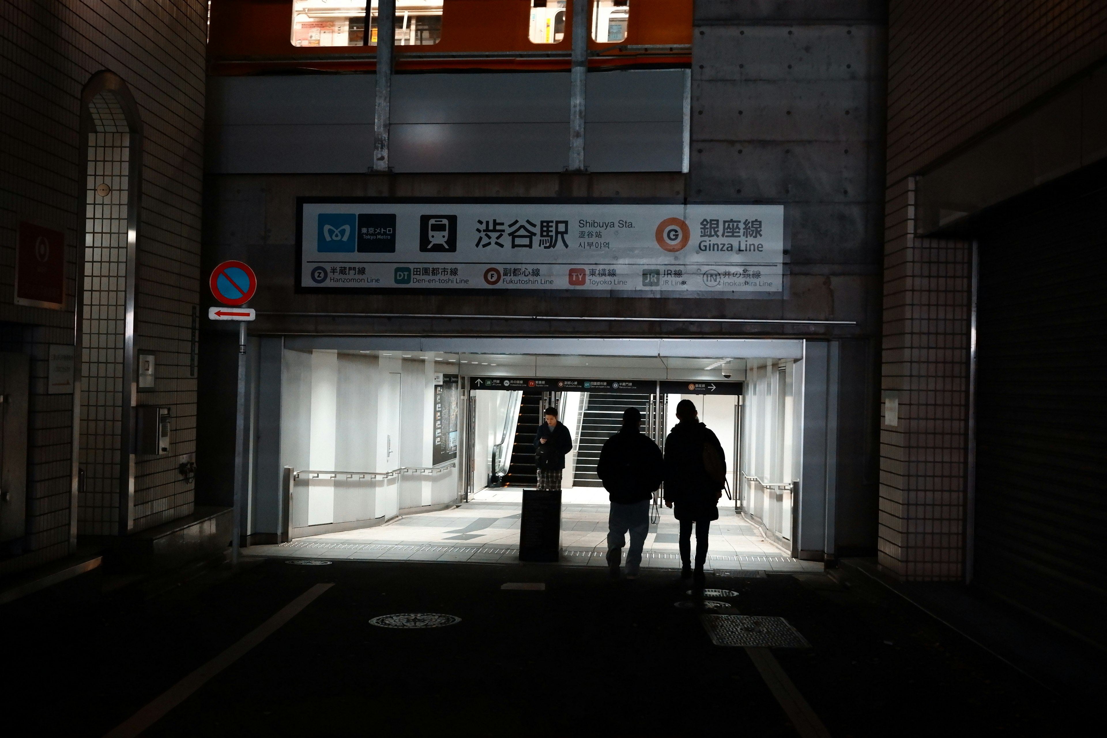 Silhouettes of two people walking through a dark passageway with bright walls