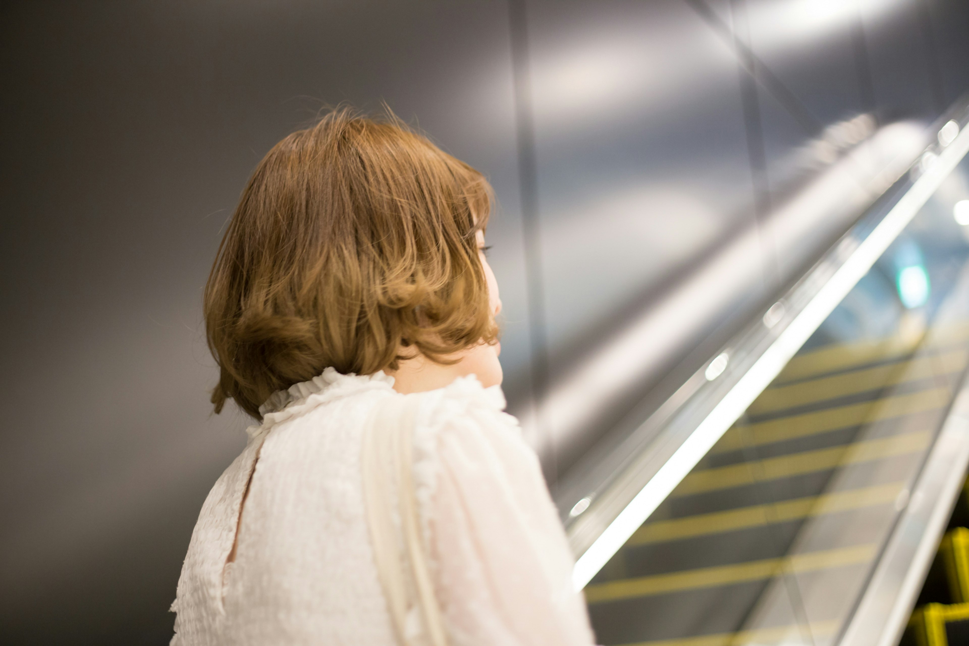 Frau, die eine Rolltreppe hinaufsteigt, mit einem Bob-Haarschnitt in einem weißen Outfit