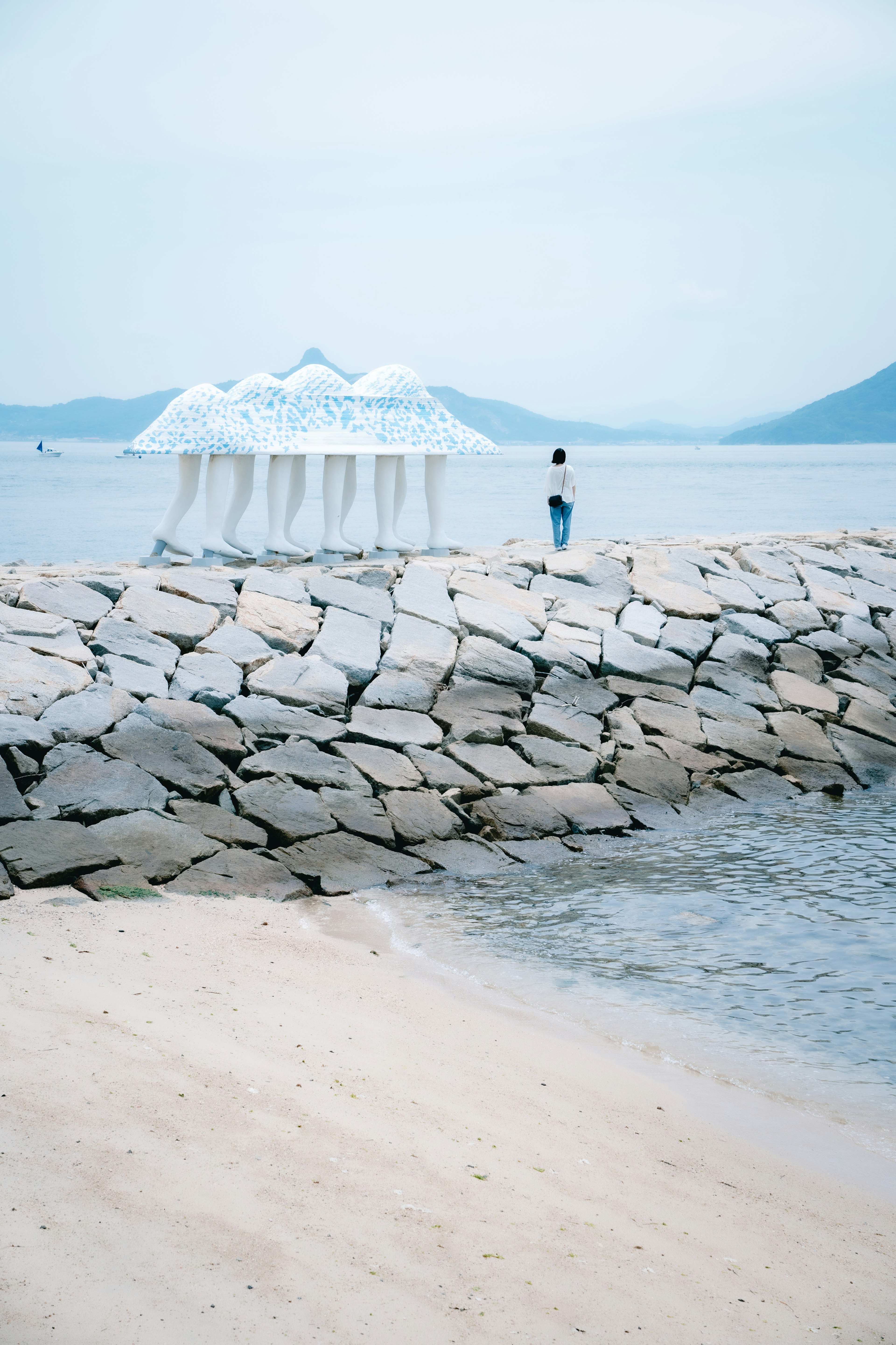 Pemandangan pantai dengan tenda putih di dermaga batu dan pantai berpasir