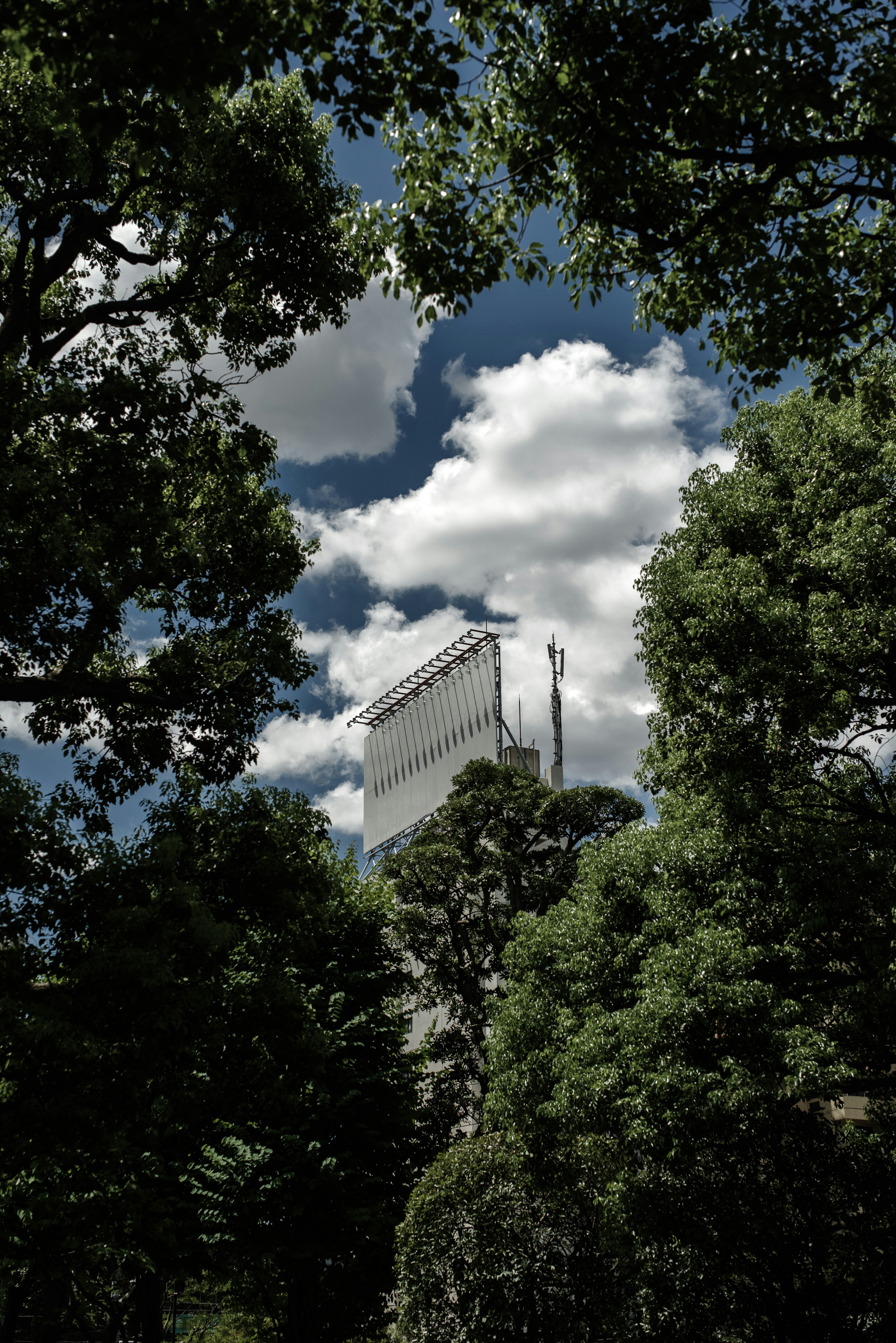 Ein Wolkenkratzer umgeben von grünen Bäumen unter einem bewölkten Himmel