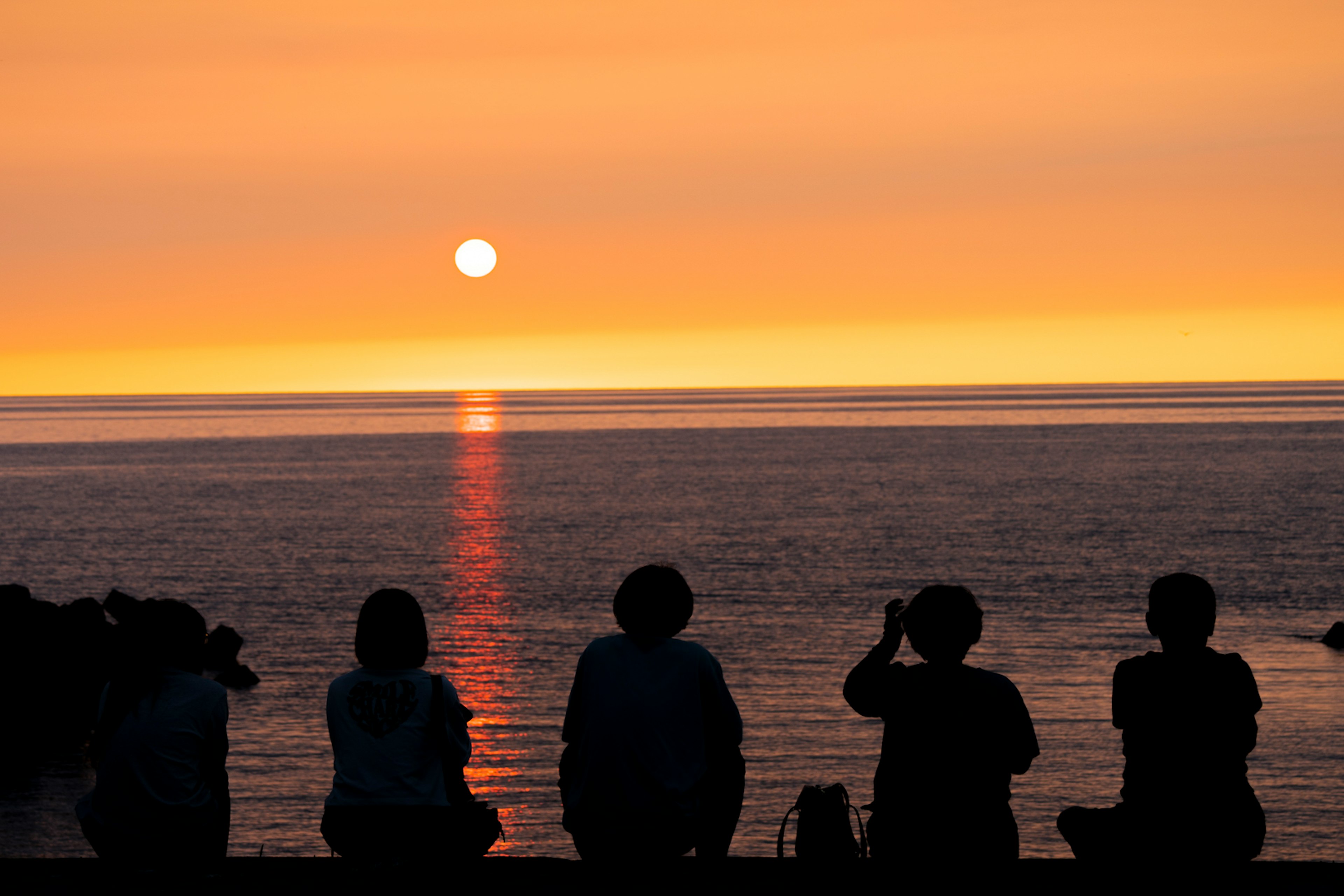 夕日を眺める人々のシルエット 海の上に広がるオレンジ色の空