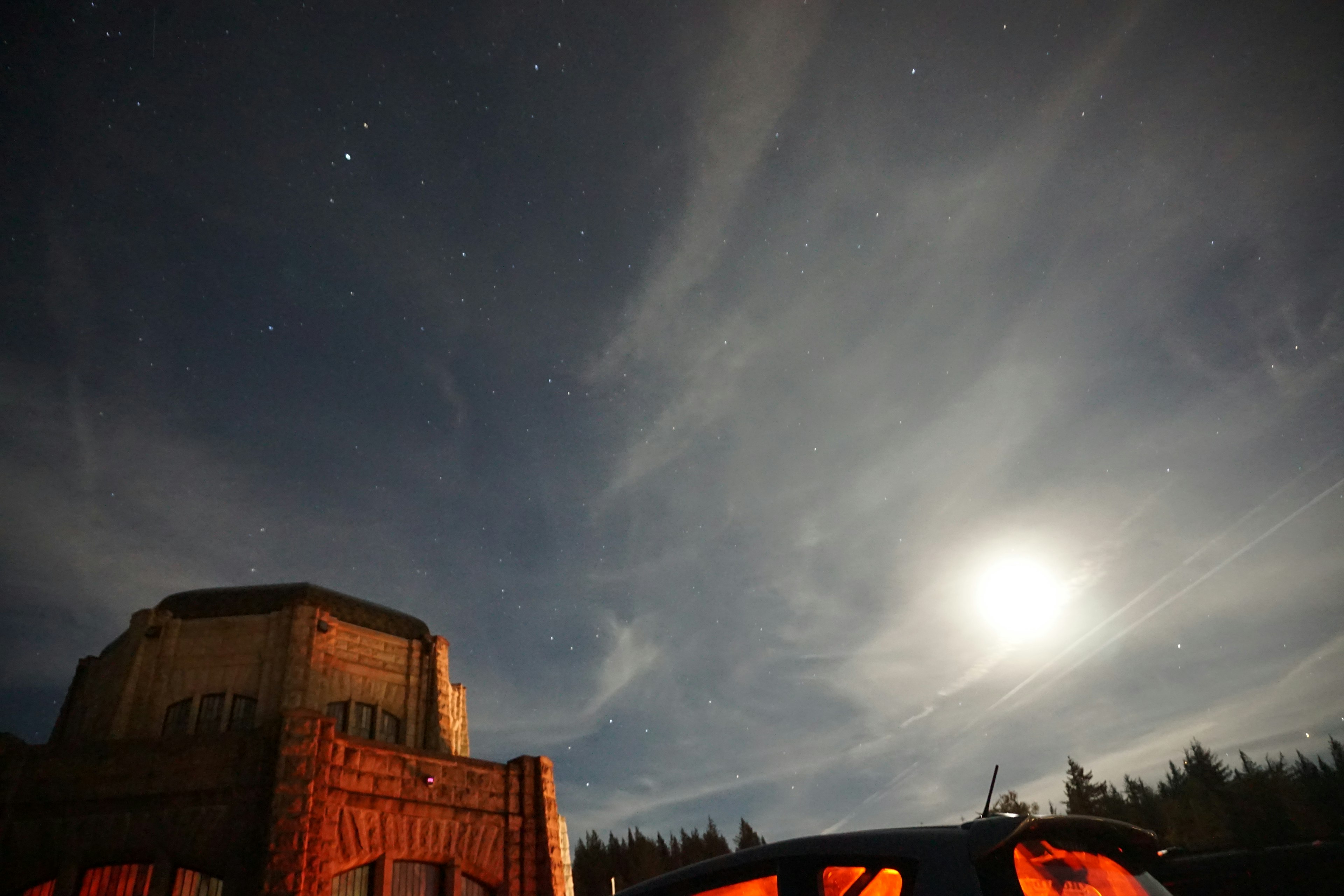 Scène nocturne avec une lune brillante et des étoiles au-dessus d'un bâtiment et d'une voiture