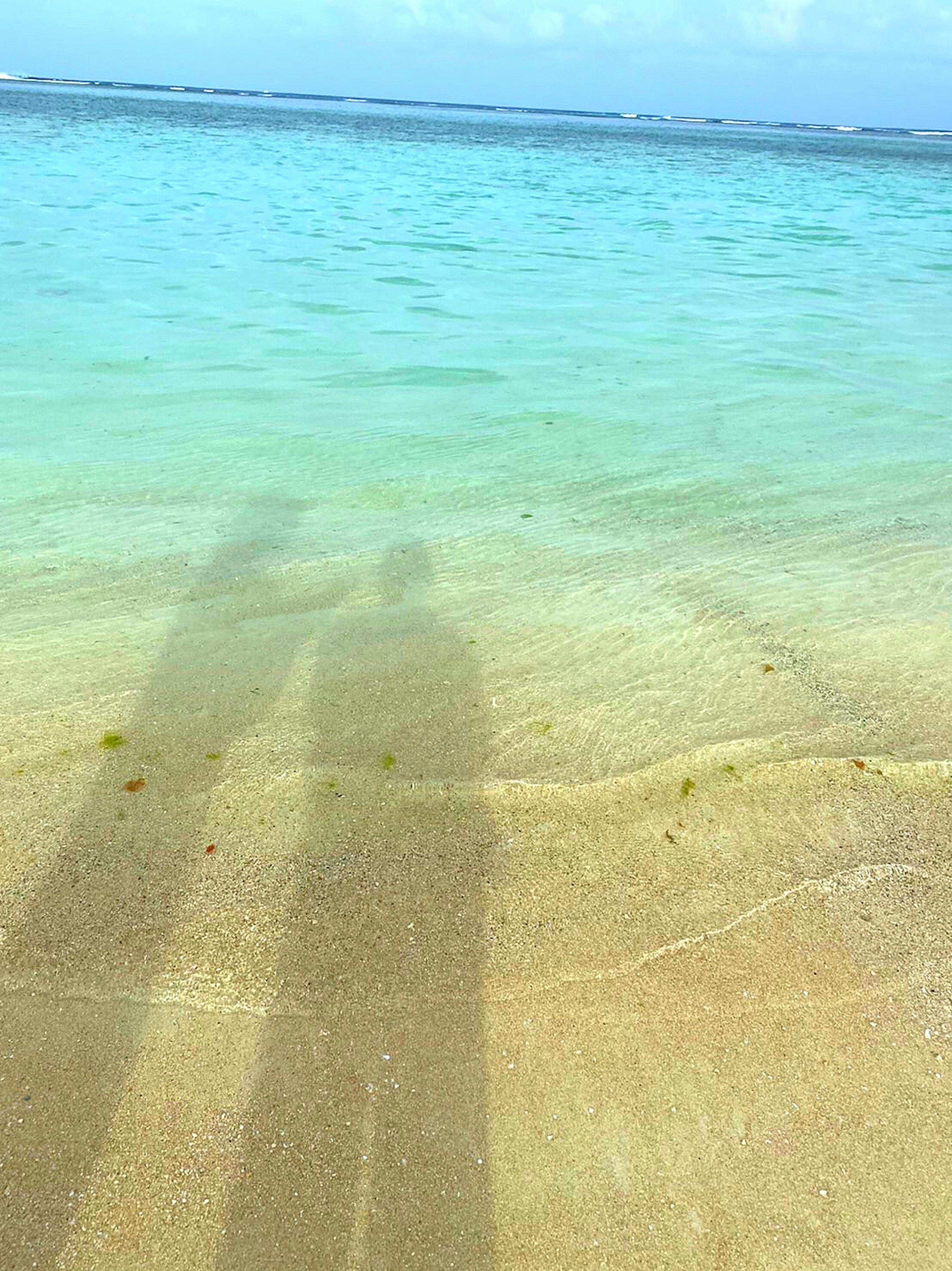 Schatten von zwei Personen an einem Sandstrand mit türkisfarbenem Wasser