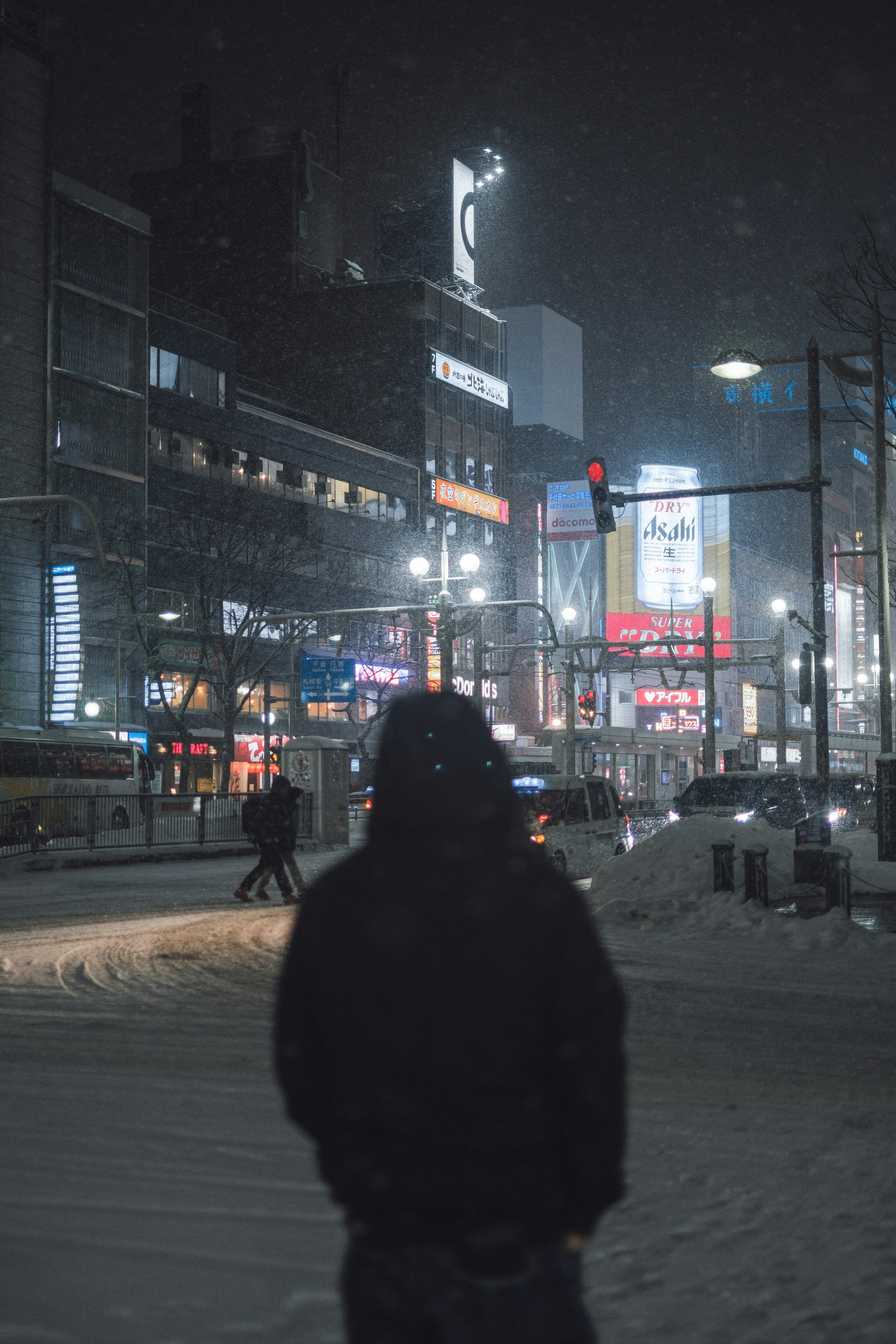 雪の降る夜の都市風景に立つ人物と明るい看板