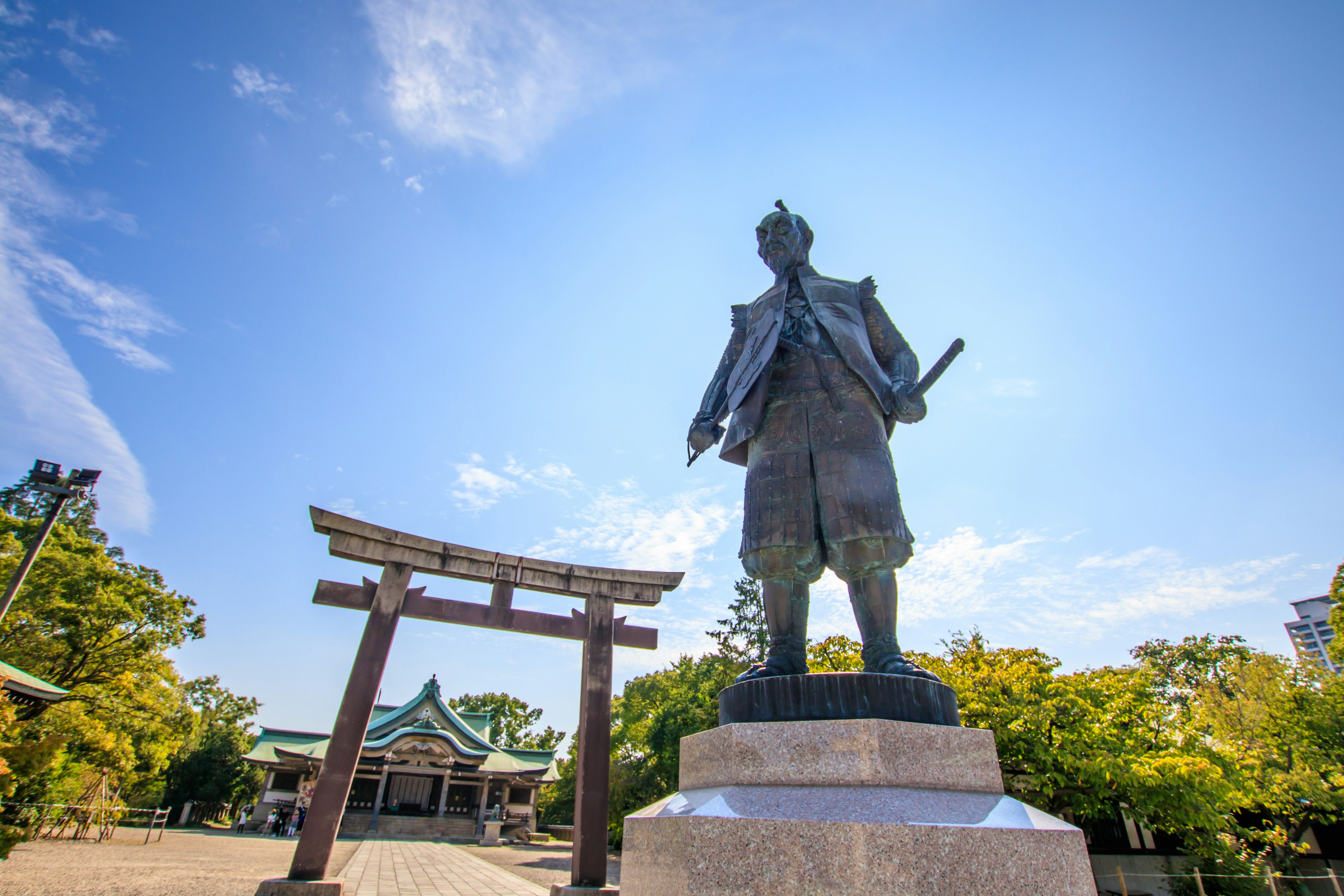 Estatua bajo un cielo azul con un torii al fondo