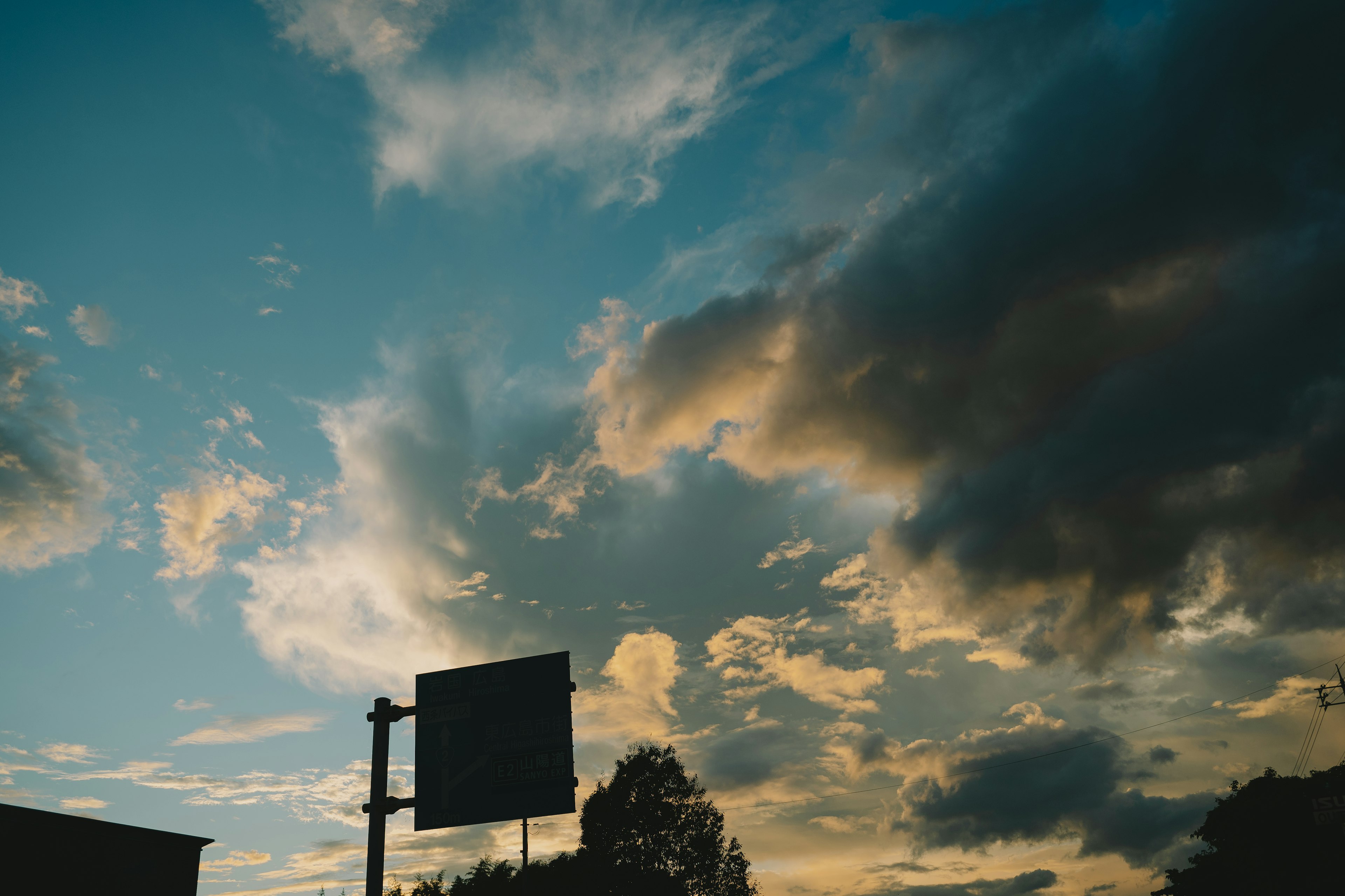 Sky filled with clouds and blue hues, sunset light illuminating a visible billboard