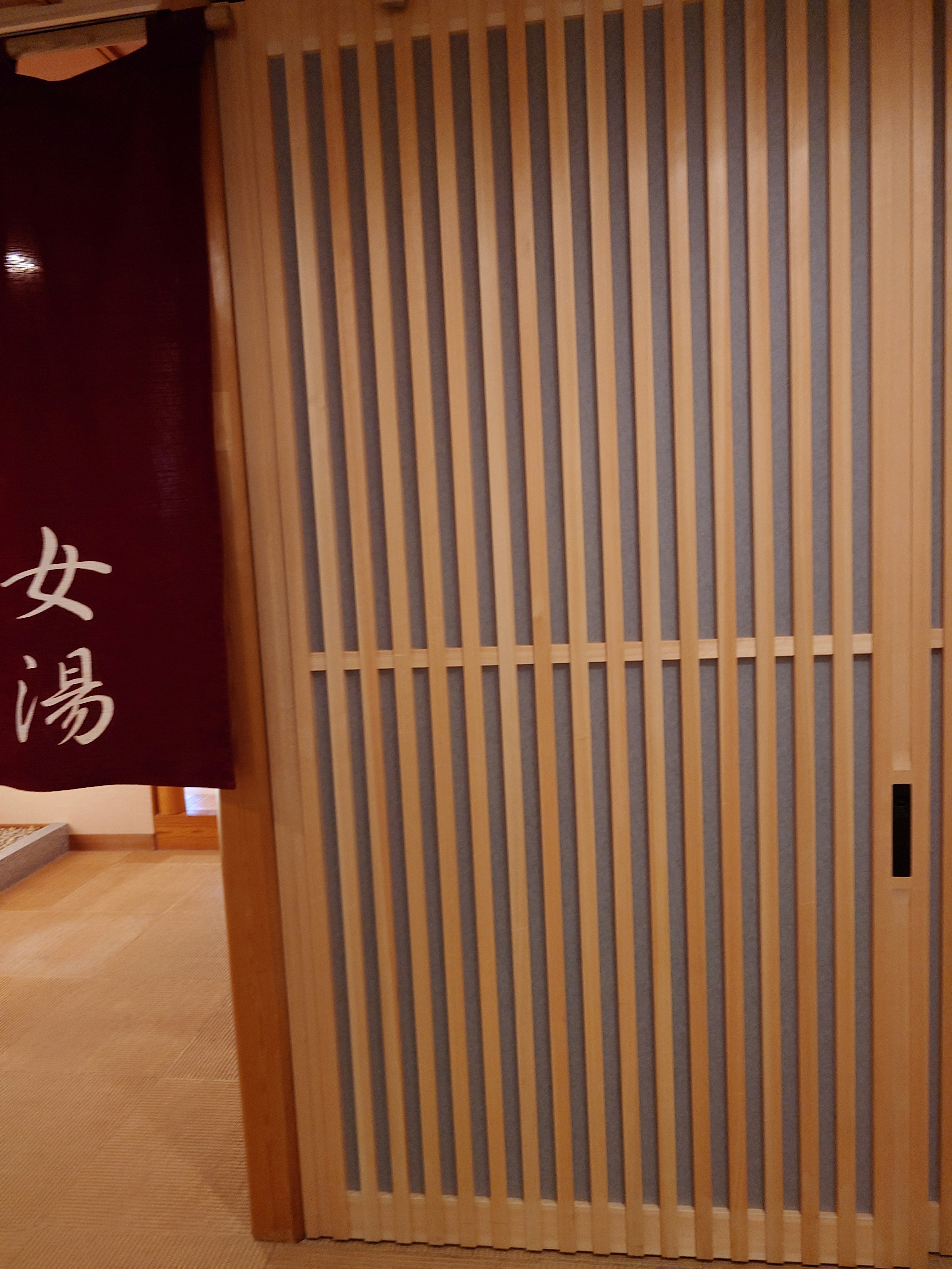 Puerta de madera con listones y noren rojo en la entrada de un onsen japonés