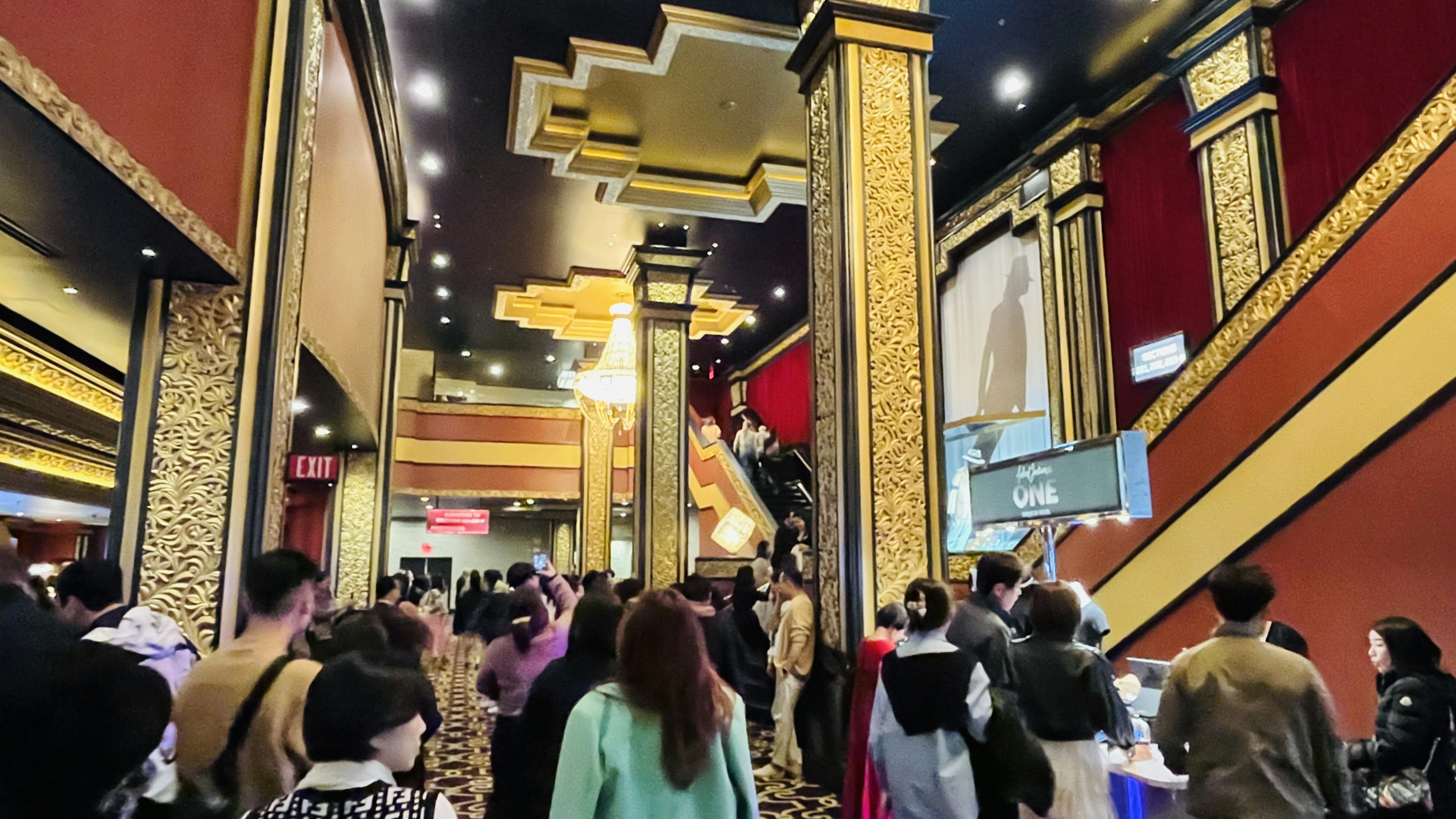 Vestíbulo de un teatro concurrido con decoración ornamental y personas tomando fotos