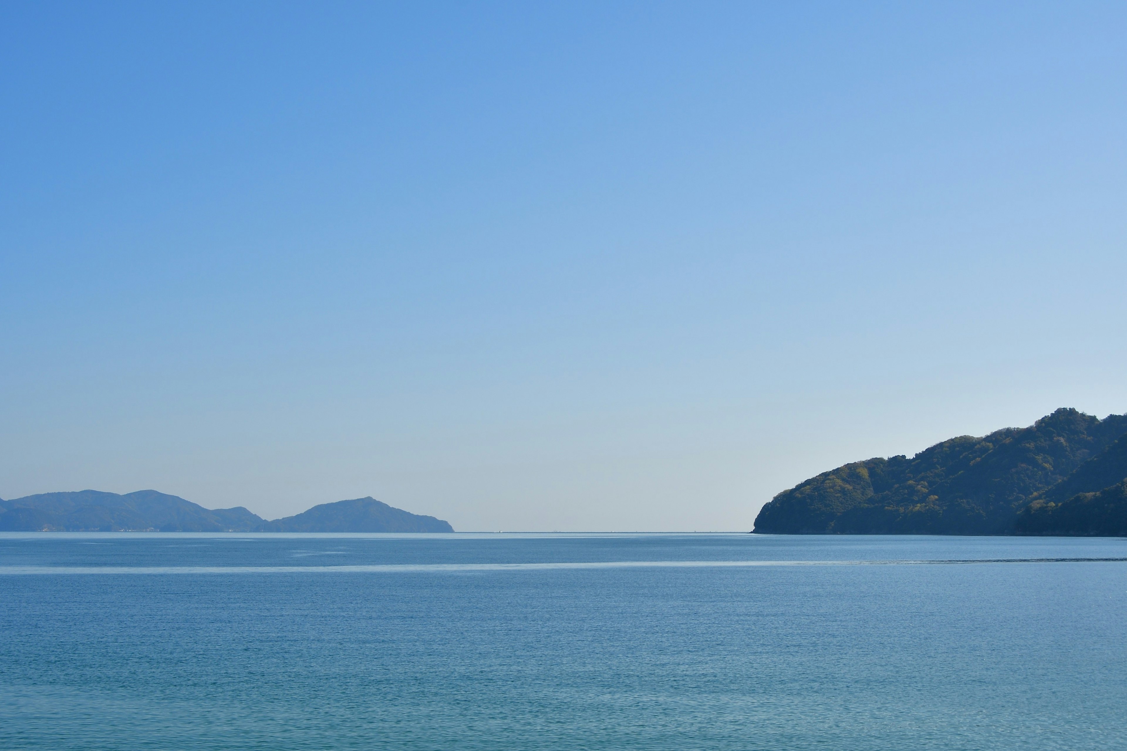 Laut dan langit biru yang luas dengan pulau-pulau kecil dan pegunungan yang terlihat