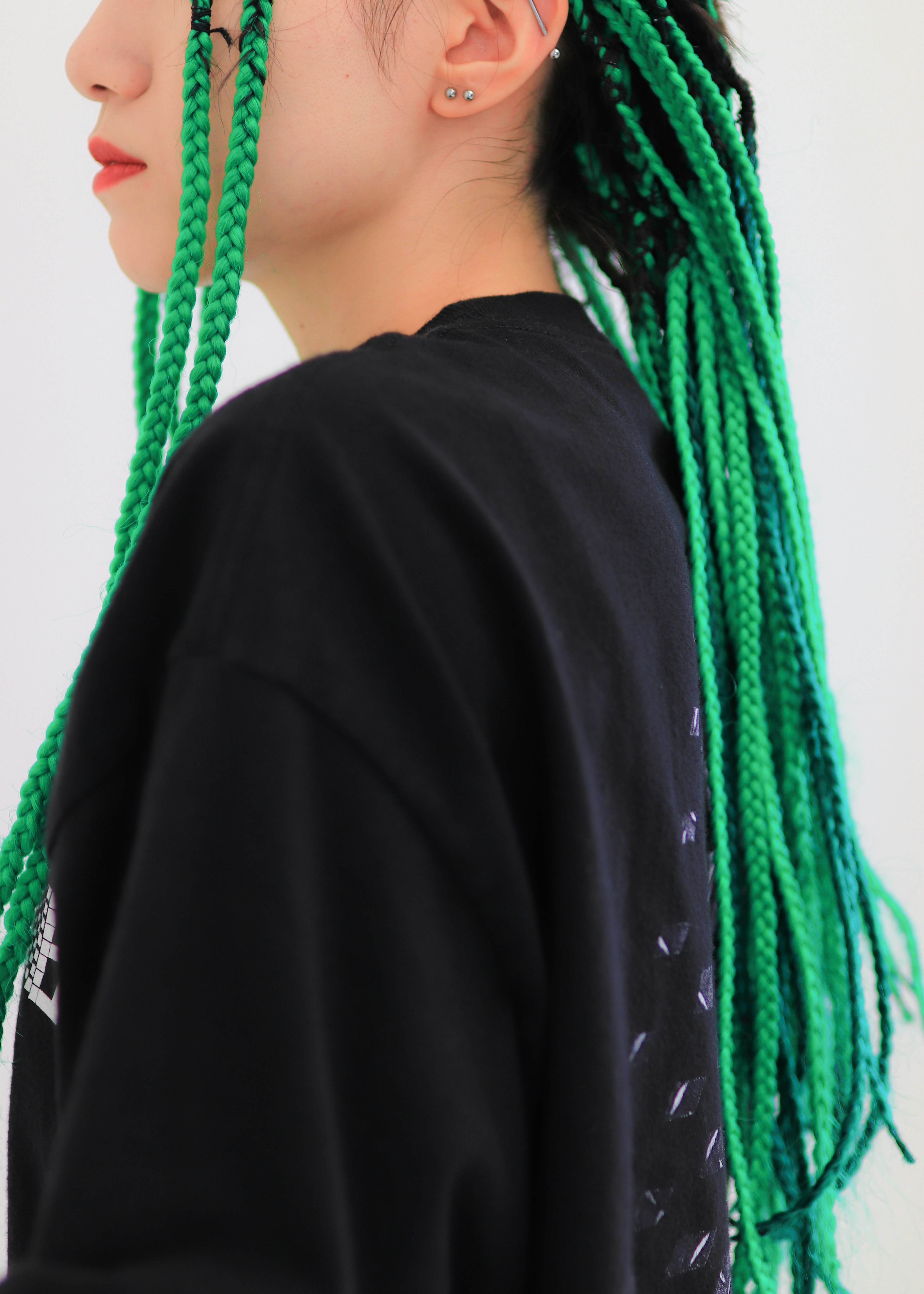 Side profile of a woman with green braided hair wearing a black sweatshirt