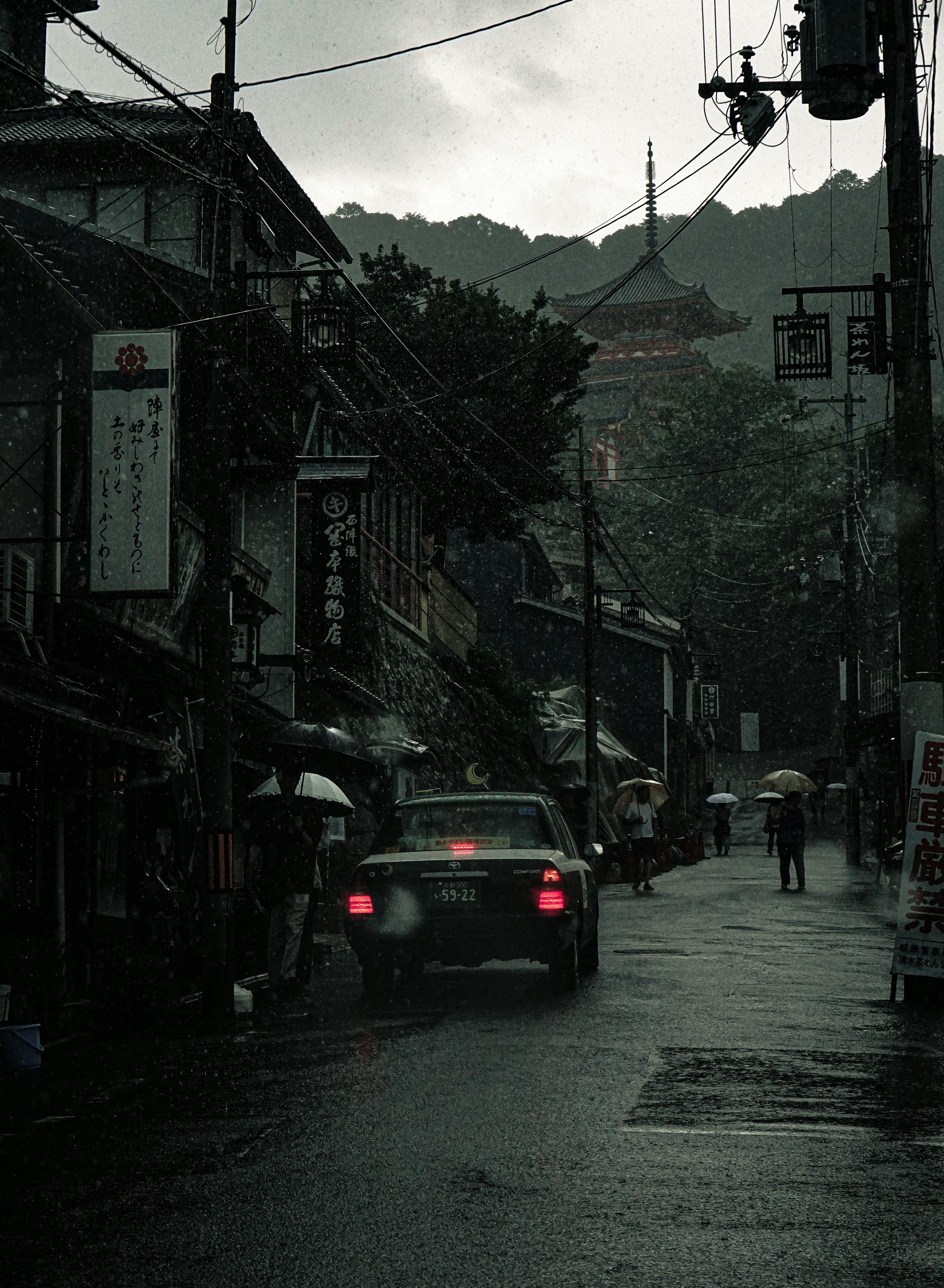 雨天街道場景，有一輛車經過商店和背景中的山