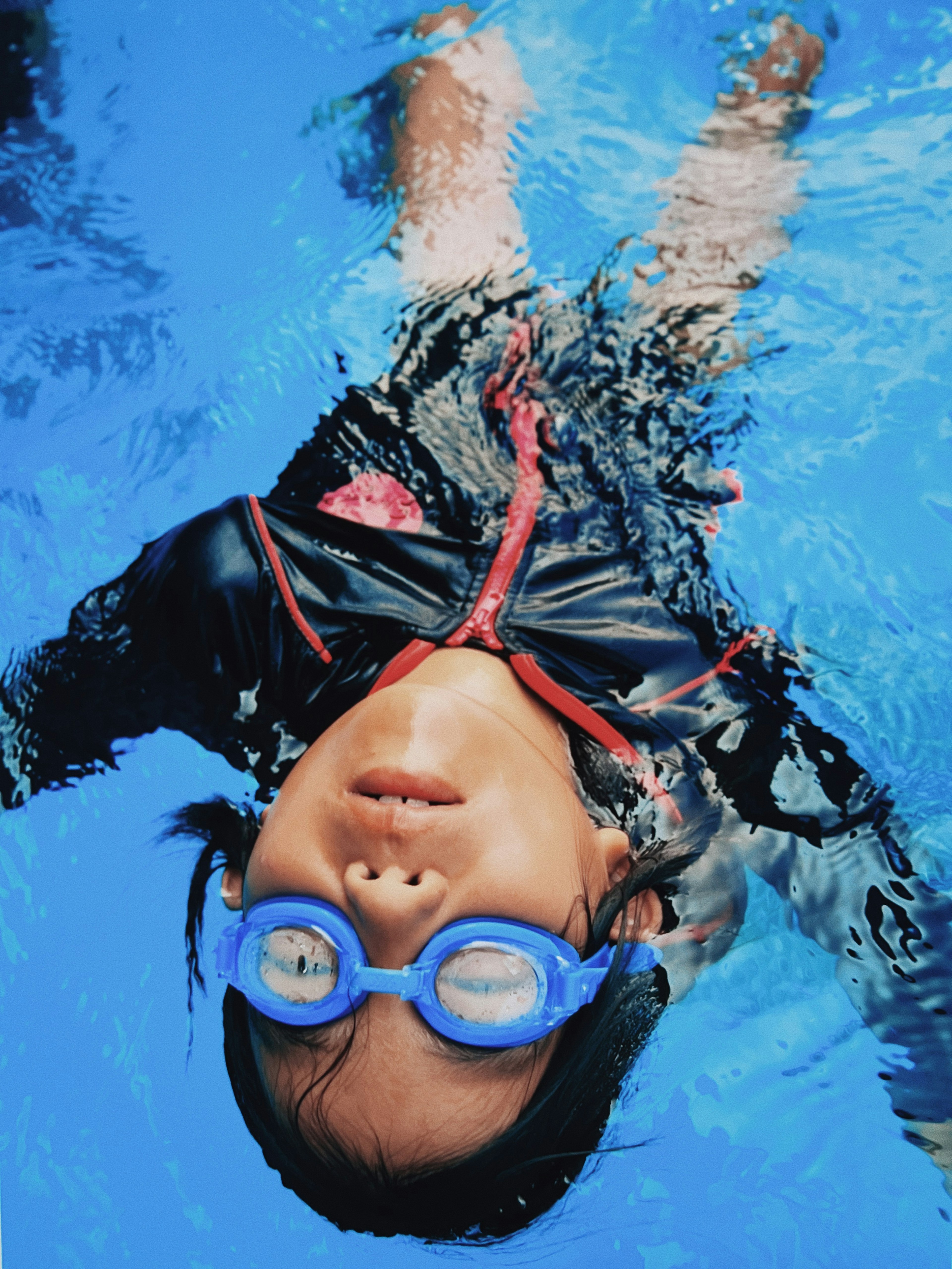 Niño nadando bajo el agua con gafas azules y traje de baño negro