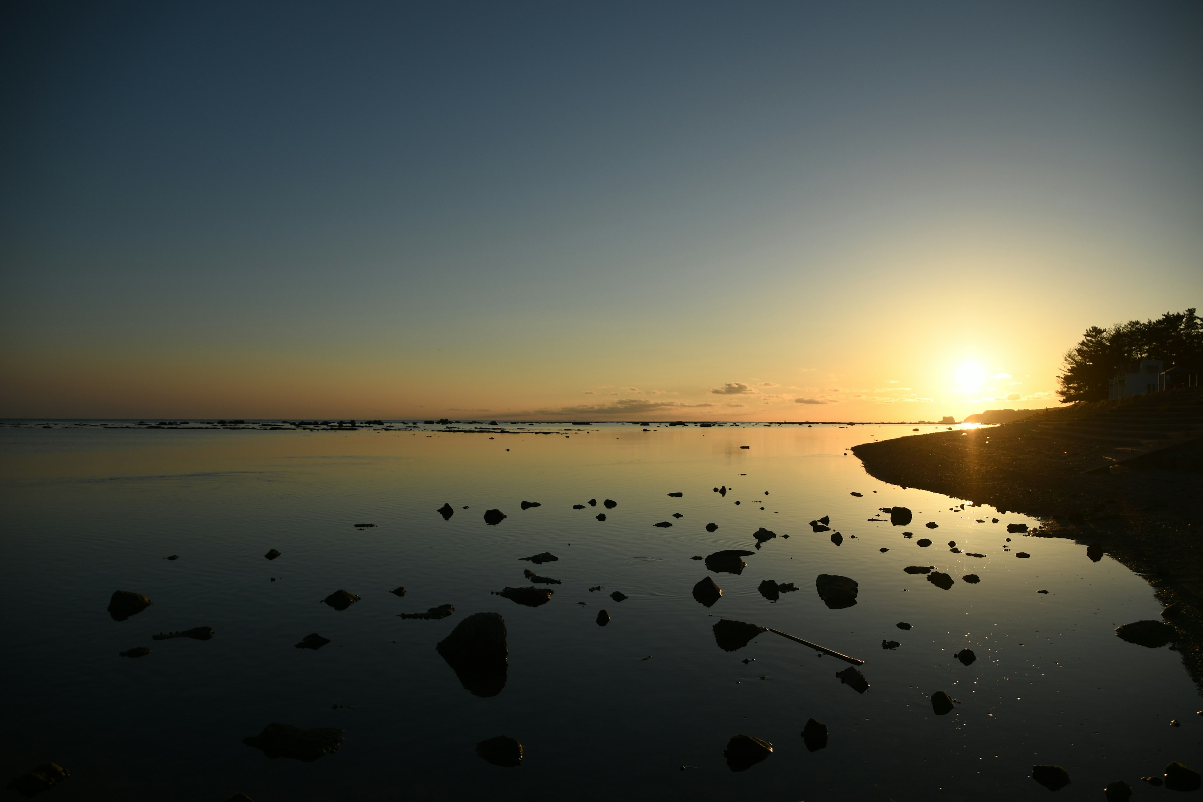 静かな海辺の夕日が反射する水面と岩