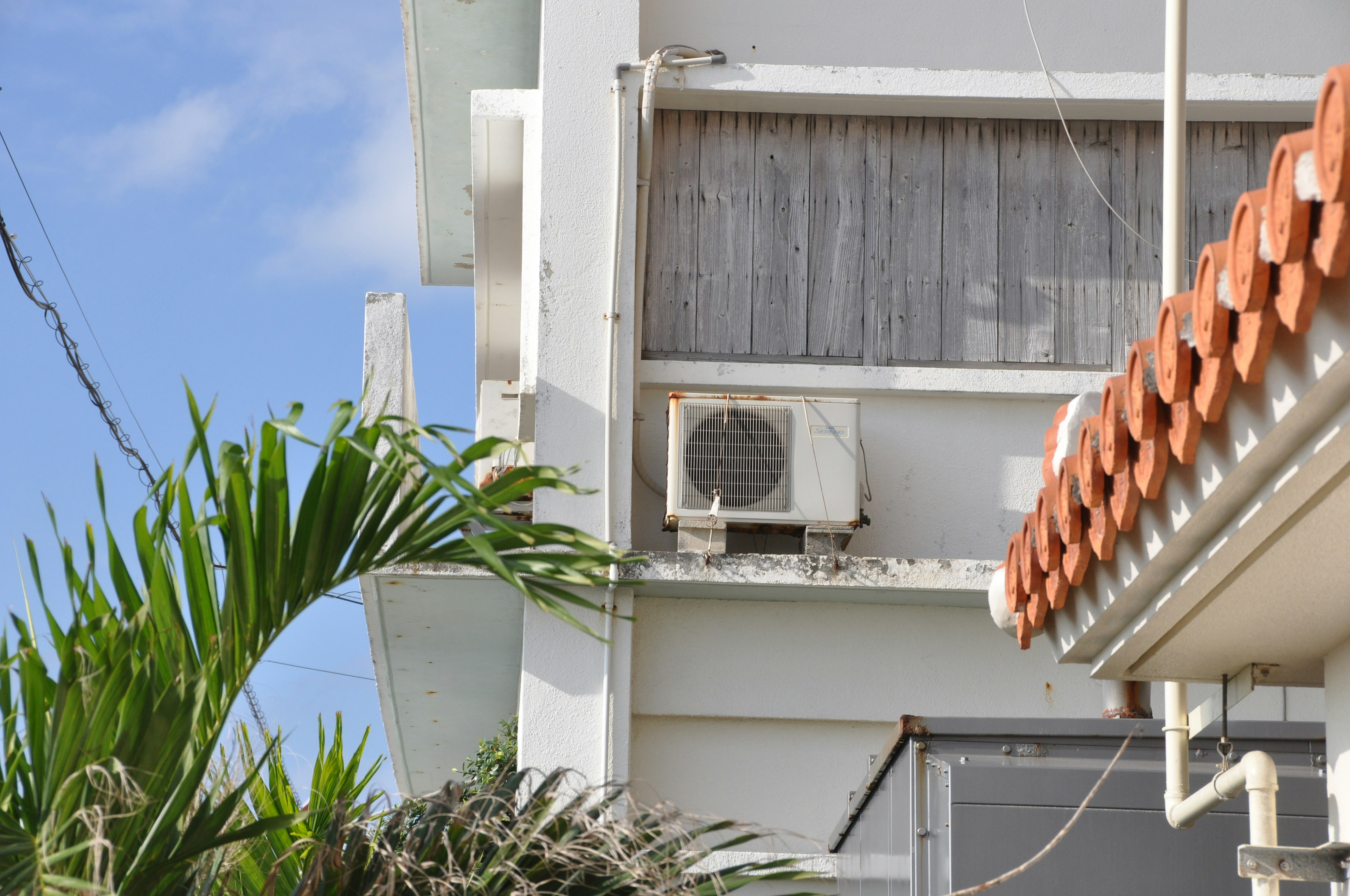 Vue latérale d'un bâtiment blanc avec une unité de climatisation et du feuillage vert