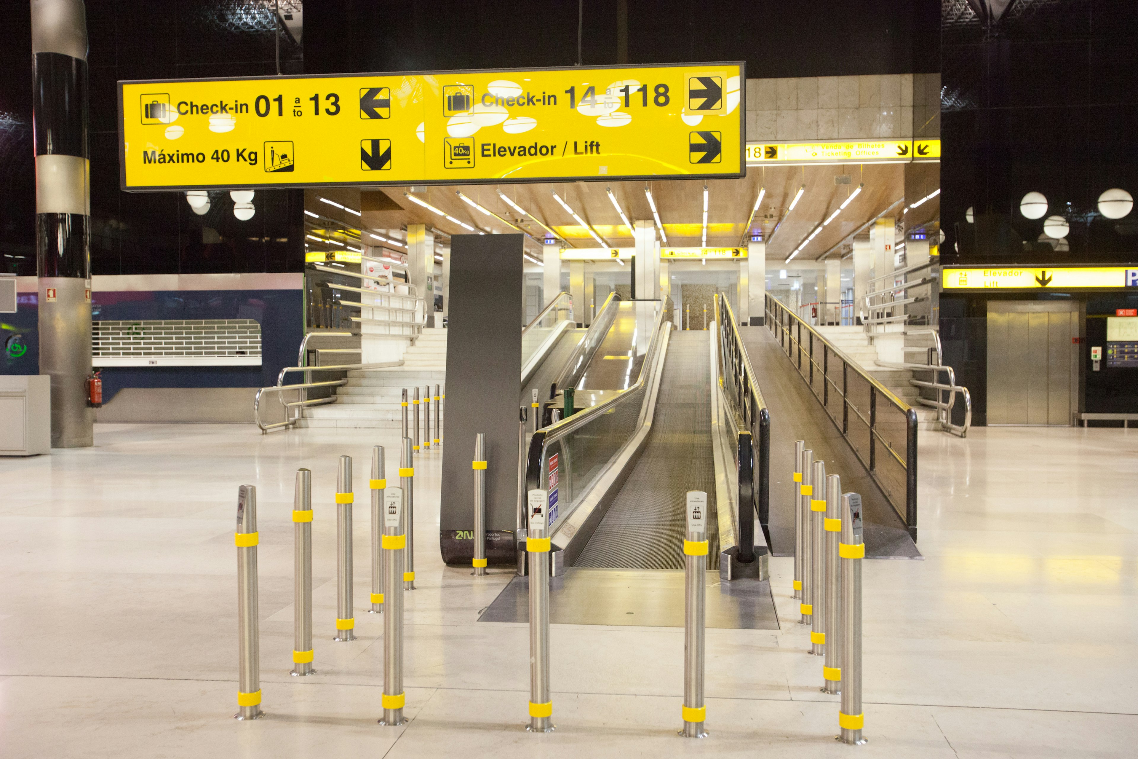 Interno dell'aeroporto con area di movimento che presenta scale mobili e segnaletica gialla