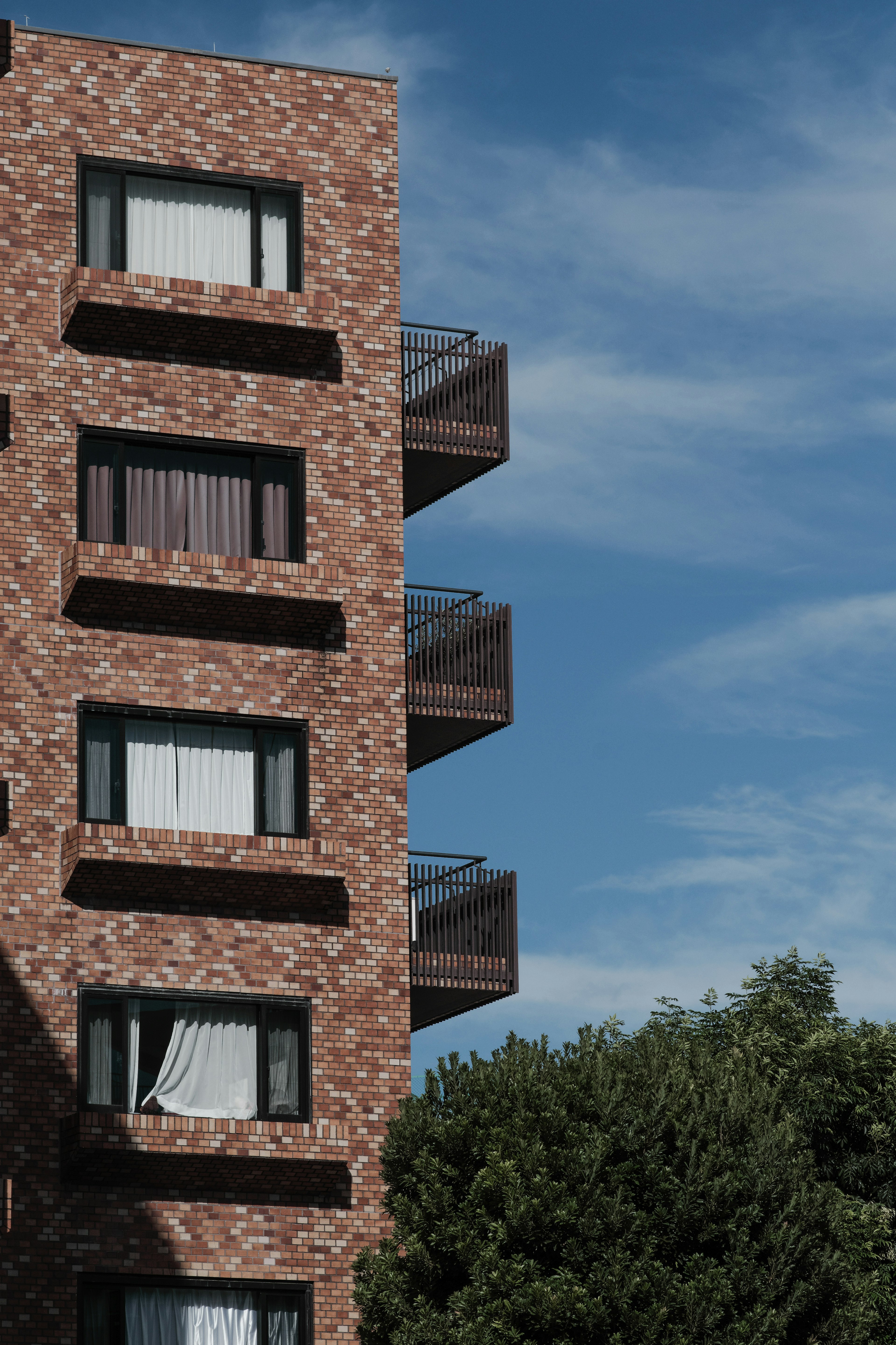 Part of an apartment building with reddish-brown brick exterior clear blue sky and green trees in the background