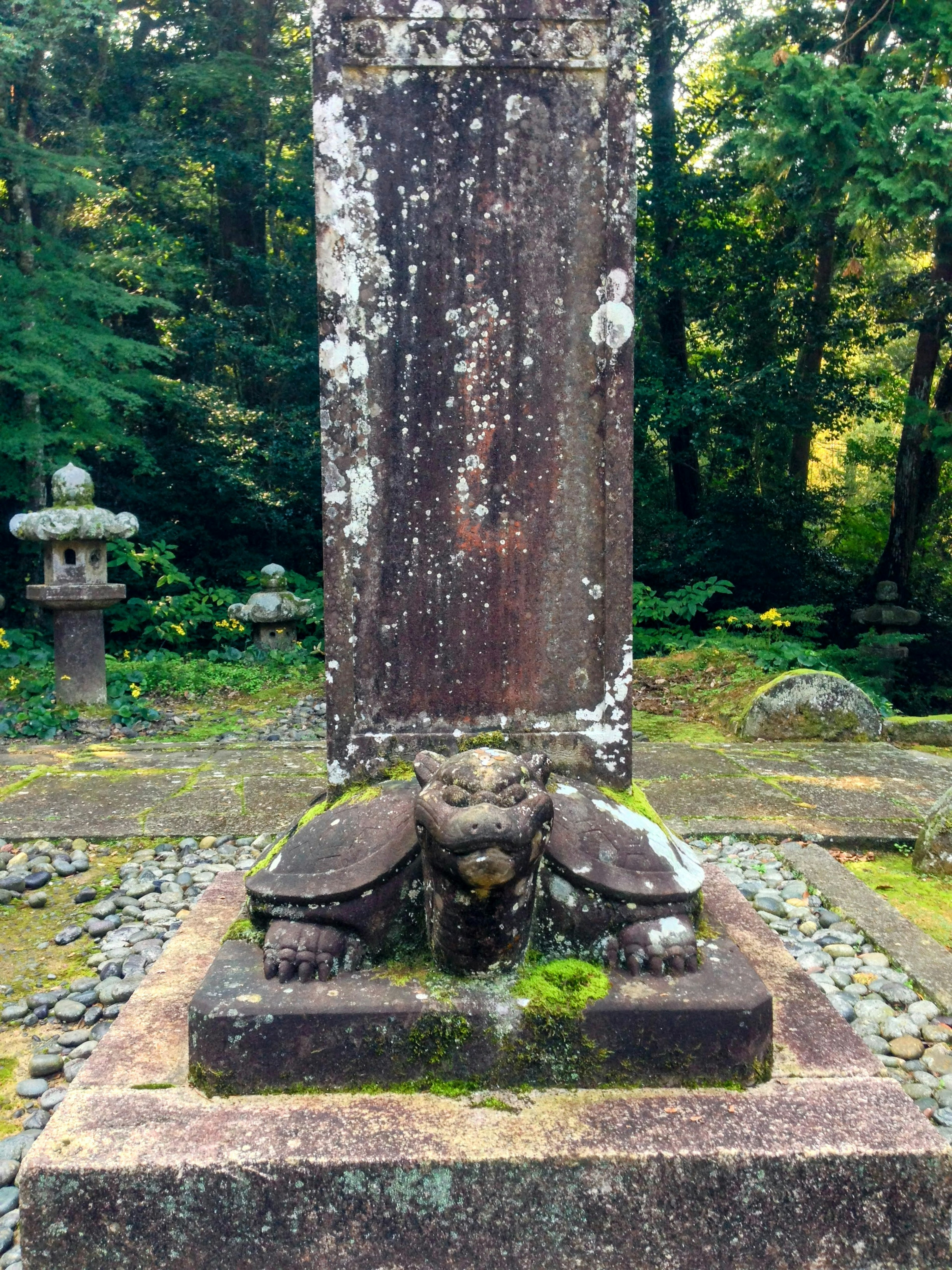 Ancient gravestone with turtle and lion sculpture covered in green moss surrounded by a tranquil forest