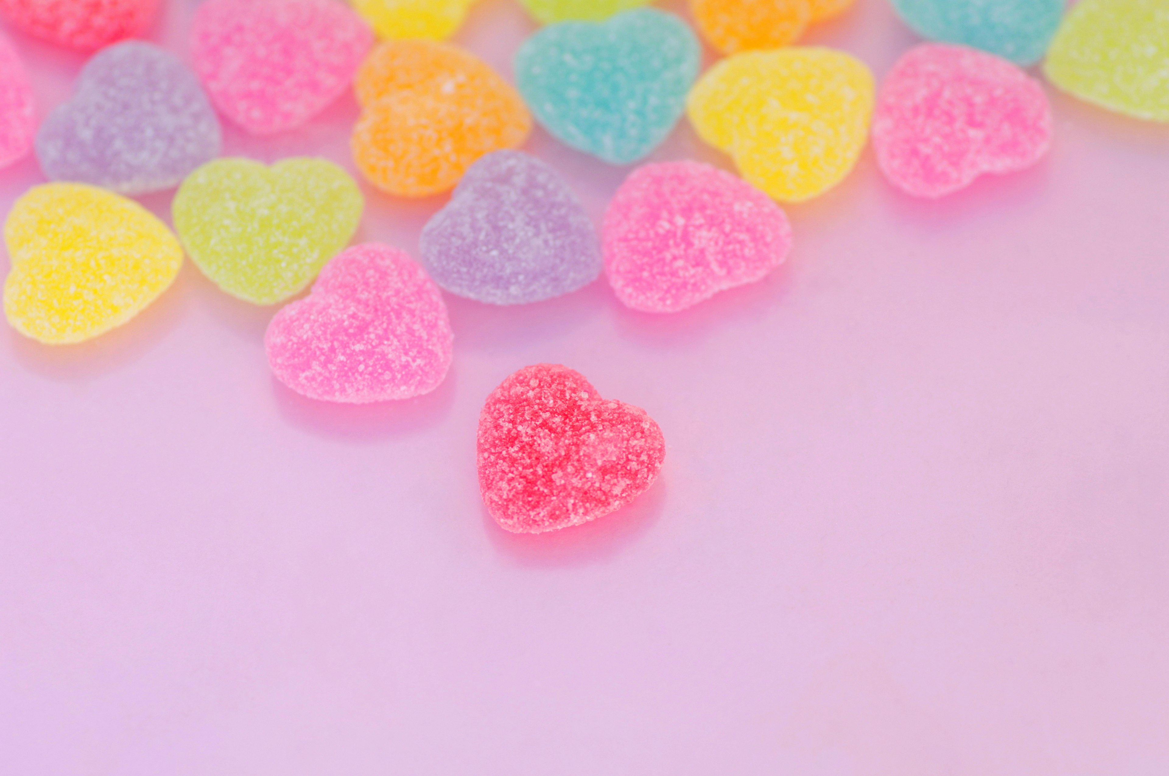 Caramelos en forma de corazón coloridos esparcidos sobre un fondo rosa