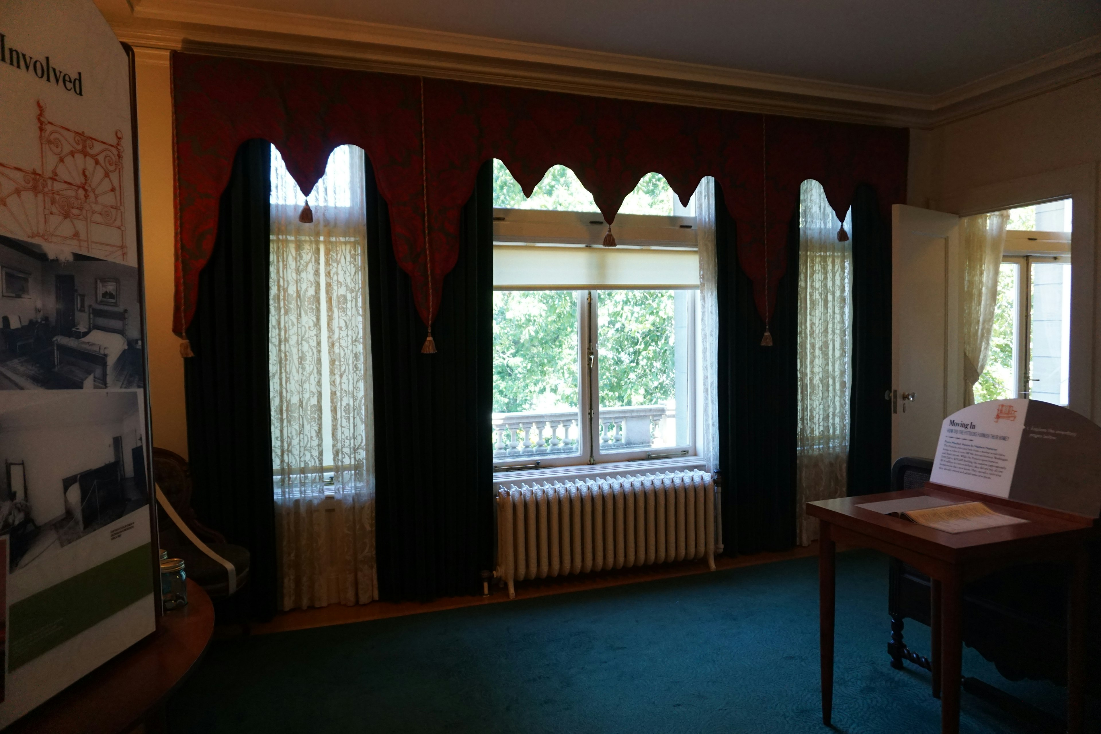 Interior de una habitación con ventana alfombra verde cortinas rojas y mesa de madera