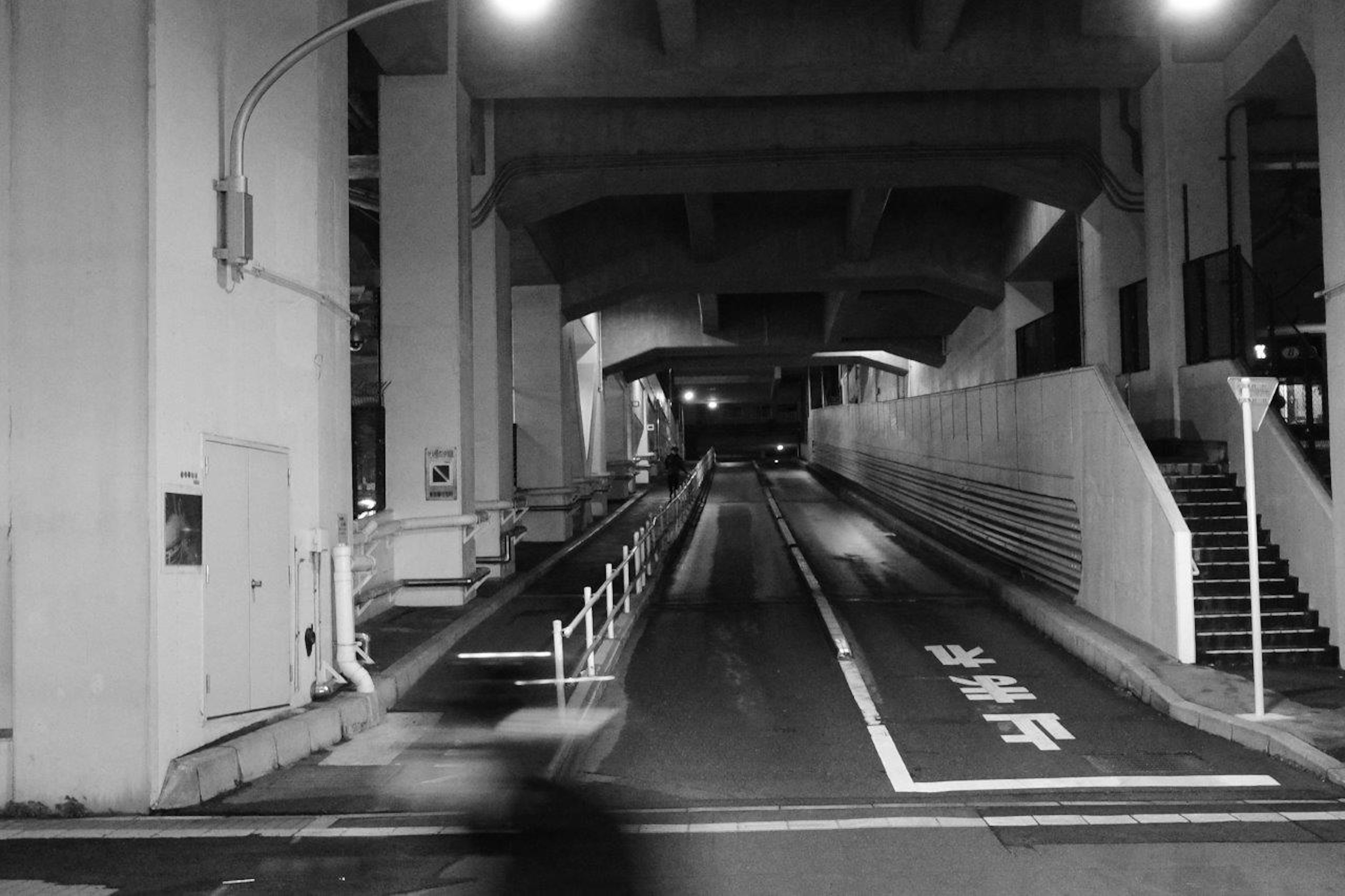 夜の都市景観のモノクロ写真 高架下の道路と階段が見える