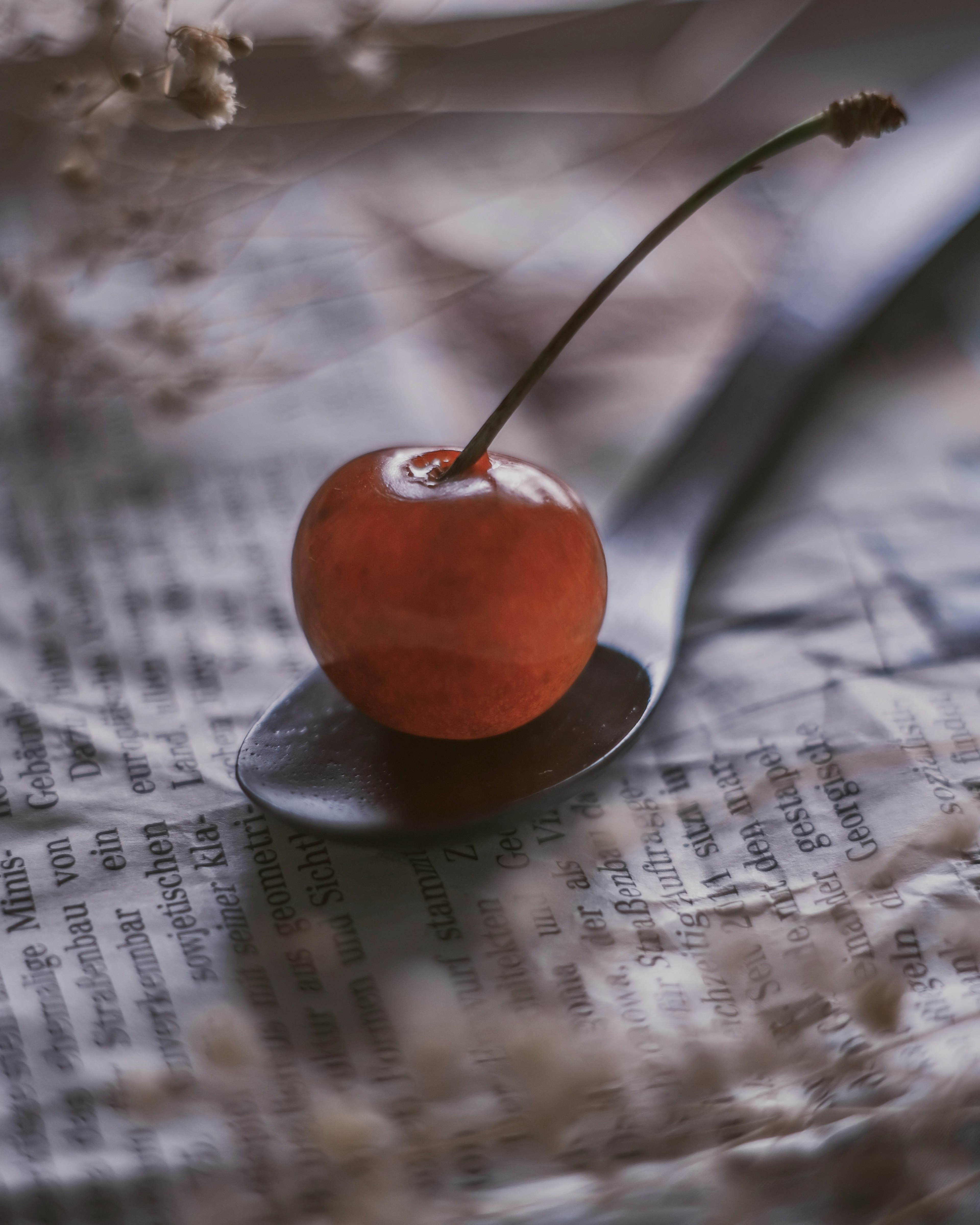 A red cherry placed on a spoon with an old newspaper background