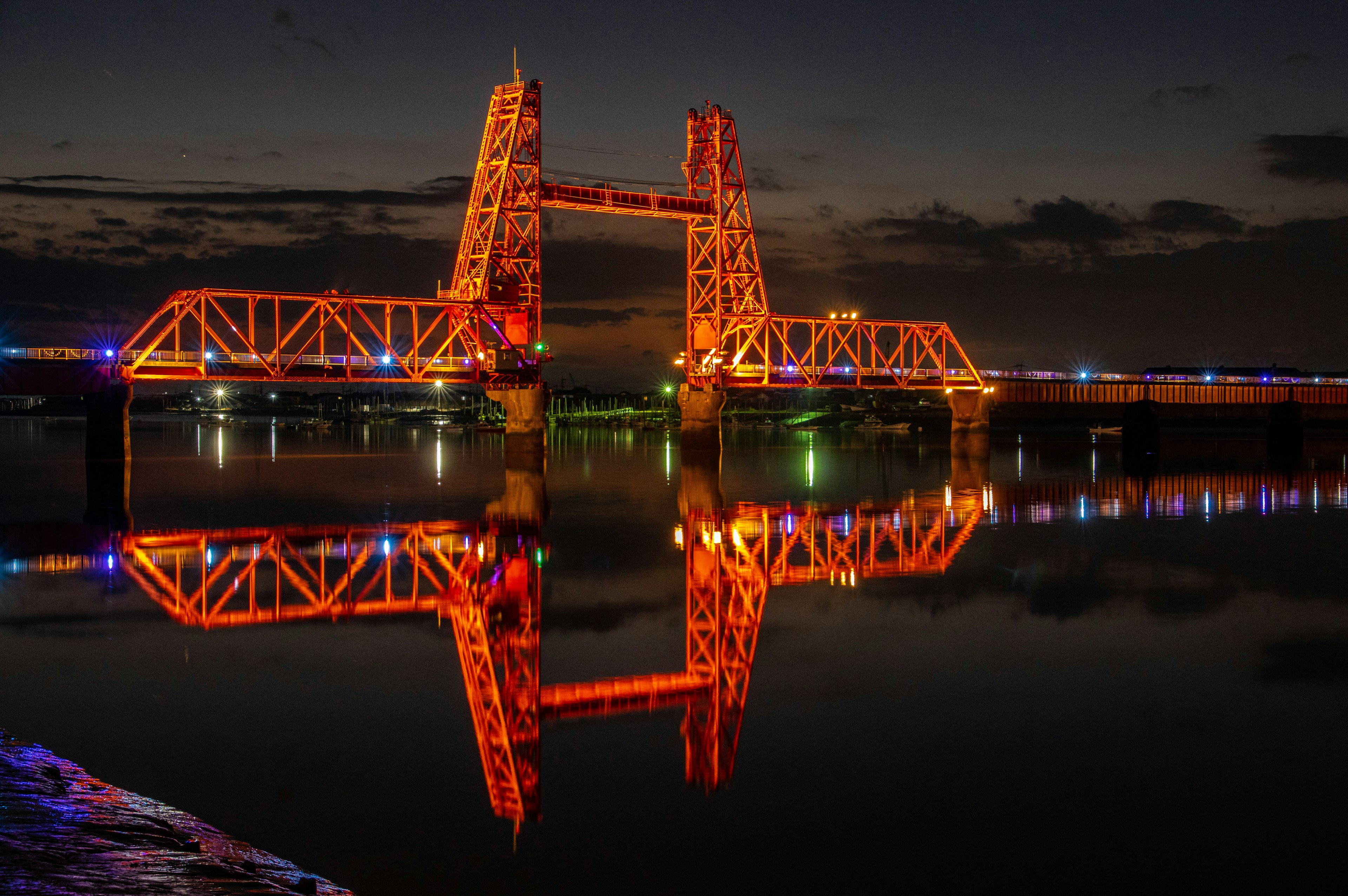 Struttura del ponte arancione che si riflette nell'acqua di notte