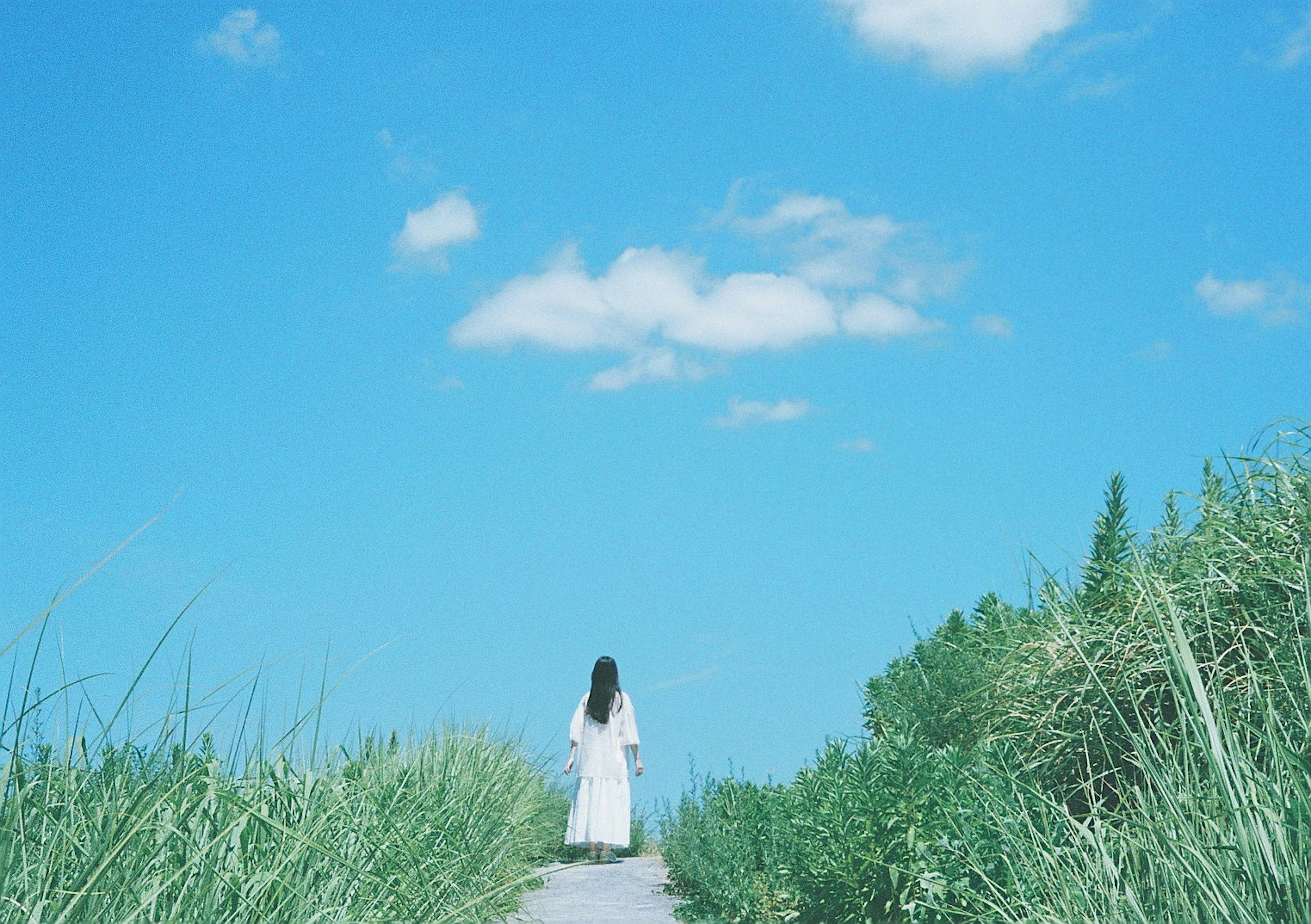 A woman in a white dress walking along a path under a blue sky