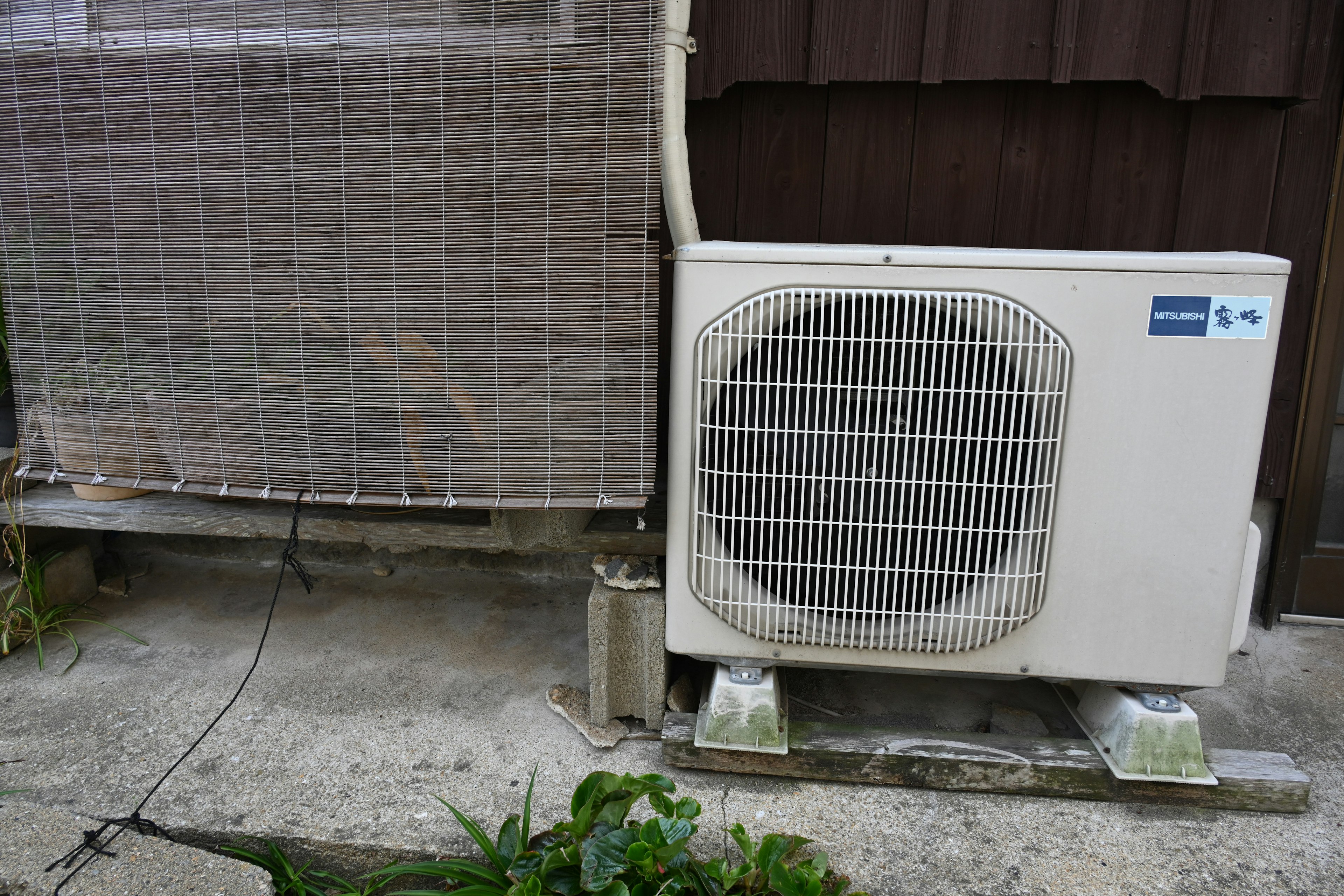 An outdoor air conditioning unit next to a wall with a nearby green plant