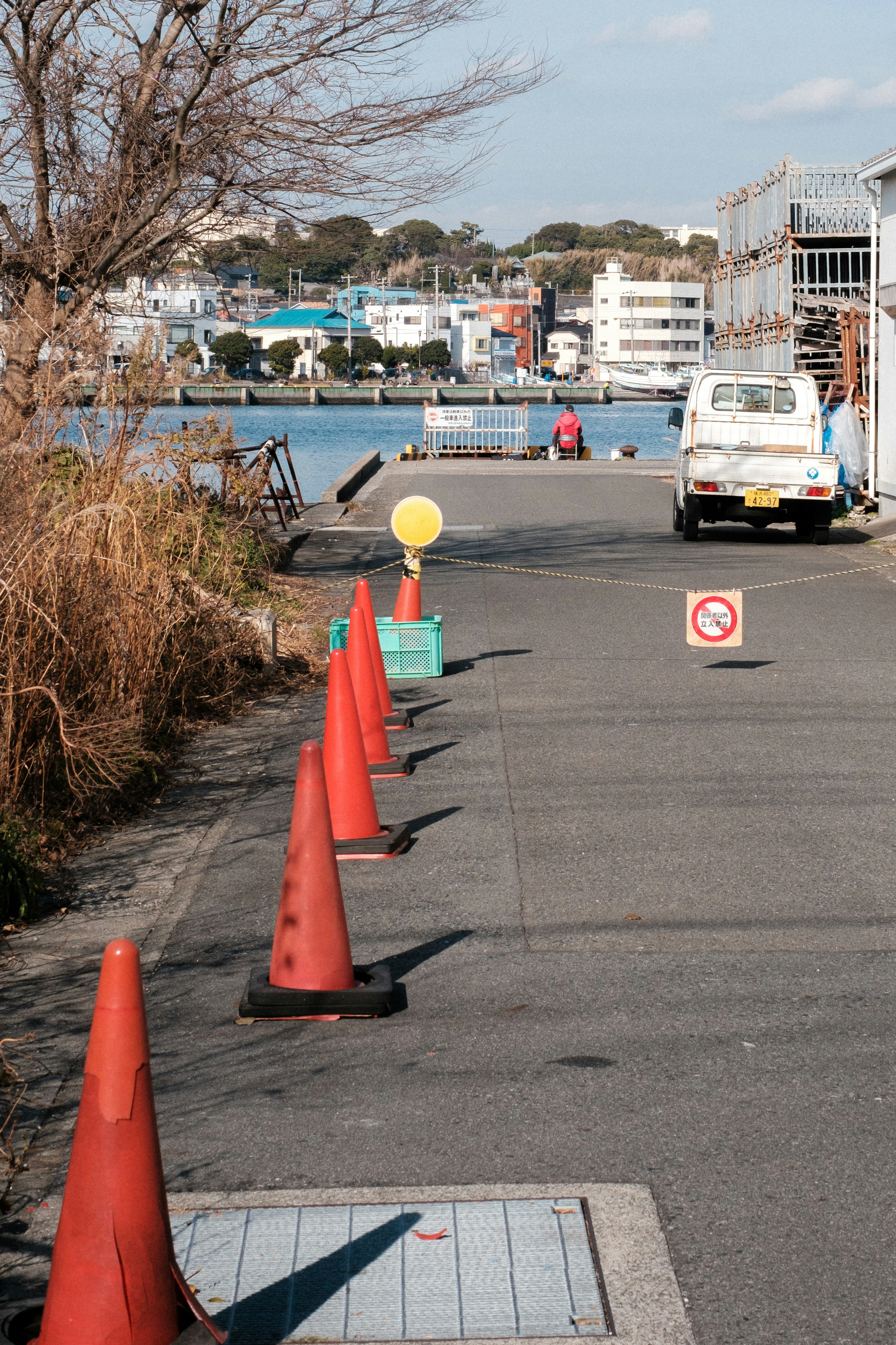 A view of a pathway lined with orange cones and a blue water body in the background