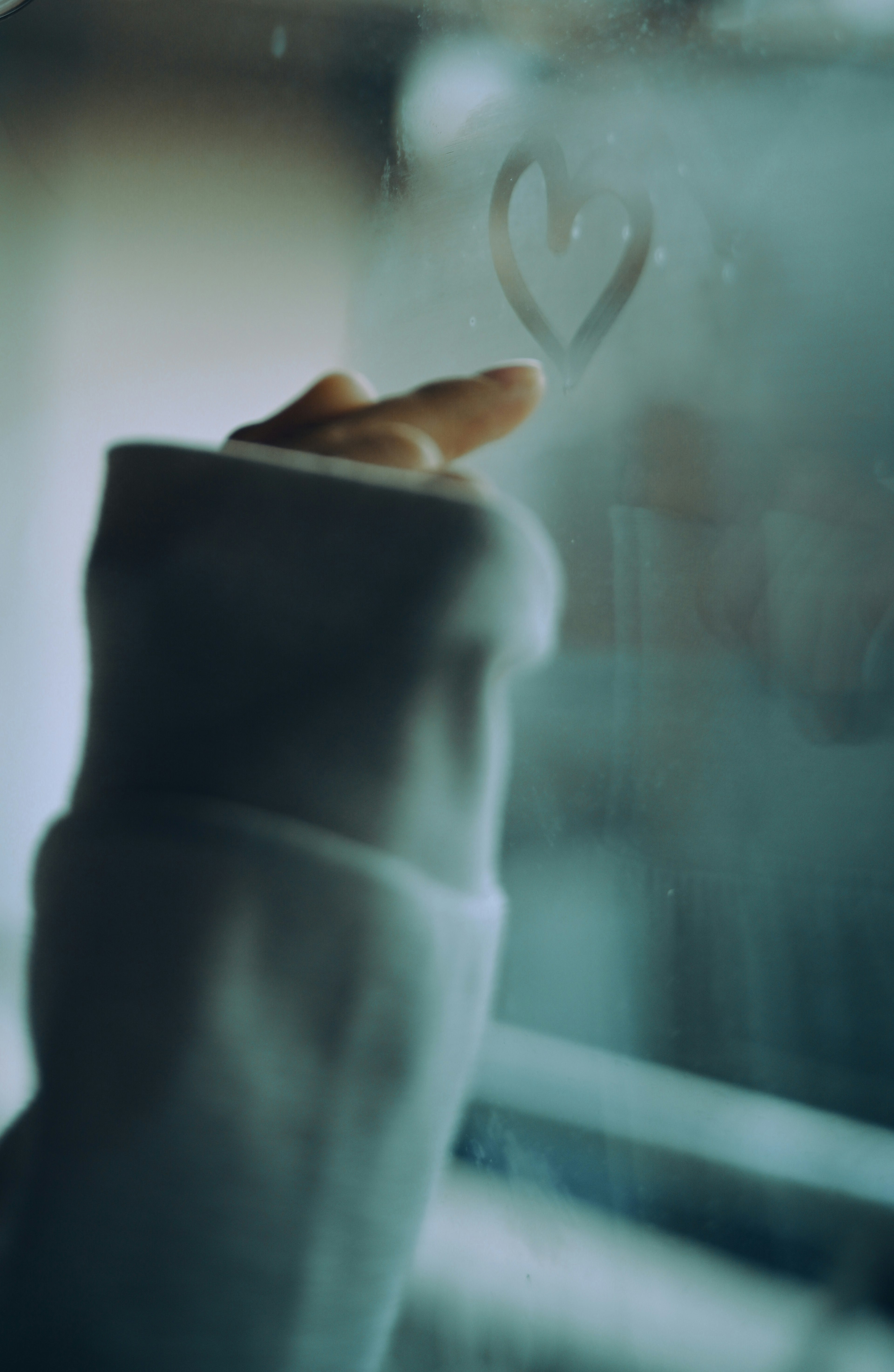 A hand drawing a heart shape on a foggy glass window wearing a sweater sleeve