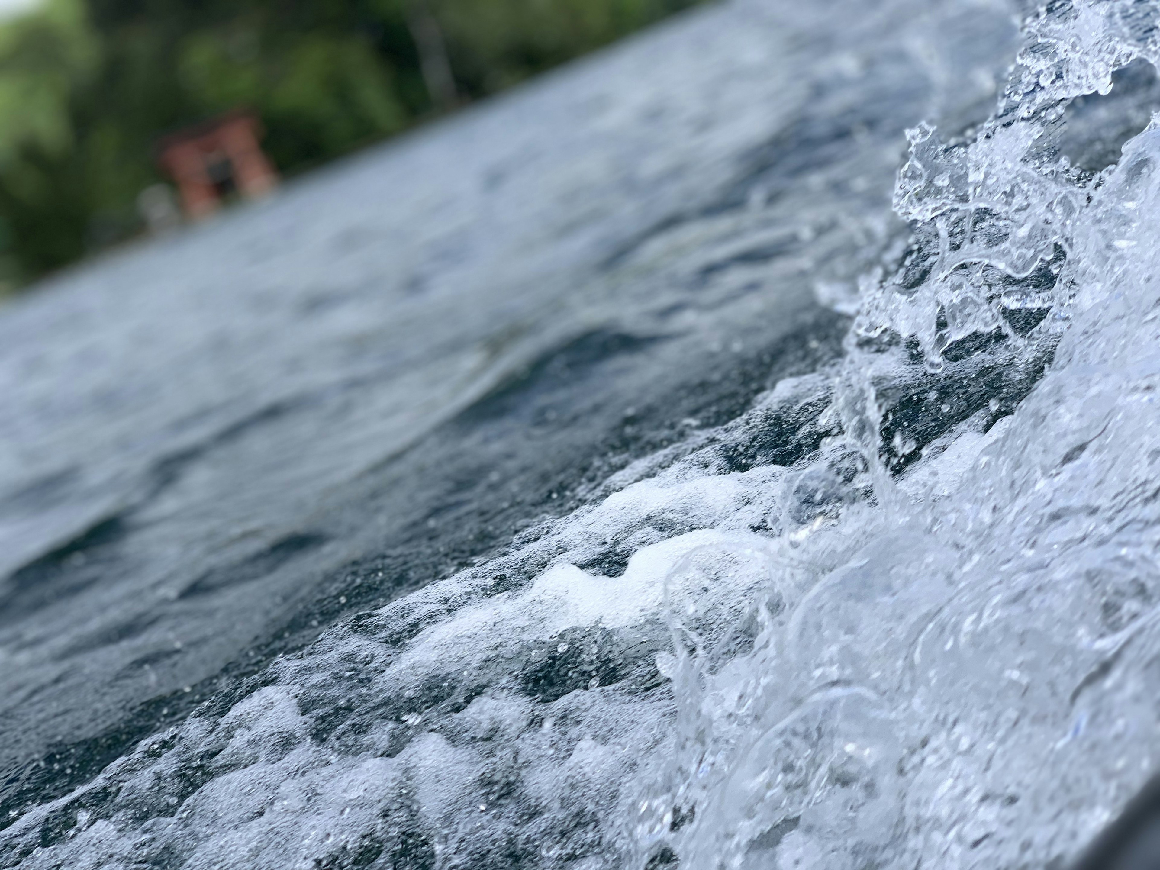 Bild zeigt Wellen und Spritzer auf dem Wasser mit grünen Bäumen und einer Hütte im Hintergrund