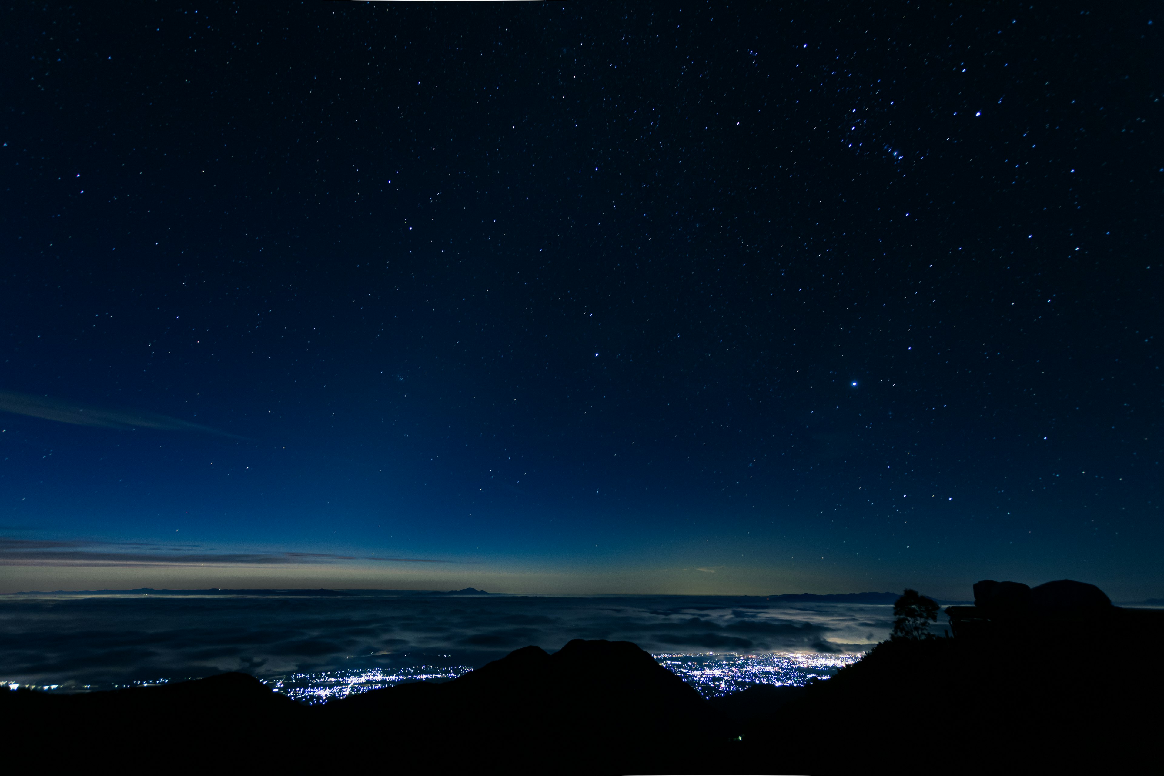 Ciel étoilé nocturne avec silhouette de montagne et lumières de la ville en dessous